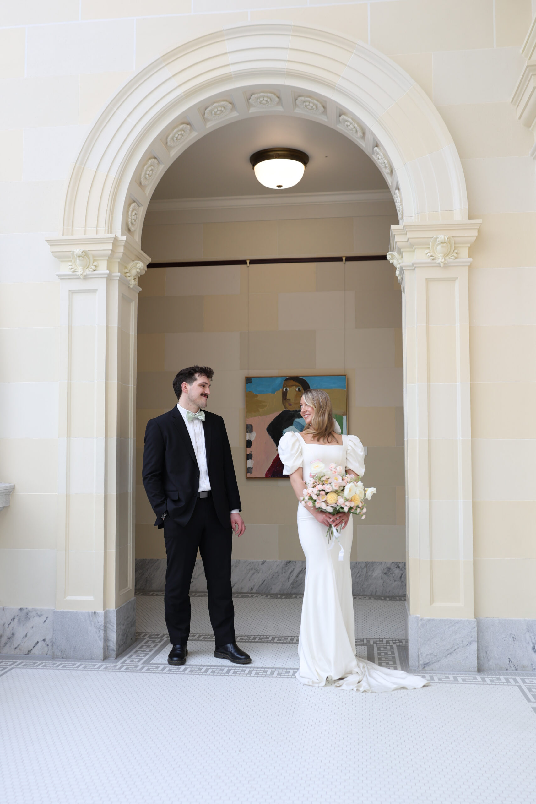 Bride and groom sharing a quiet moment in a marble hallway arch, bride holding pastel wedding bouquet.