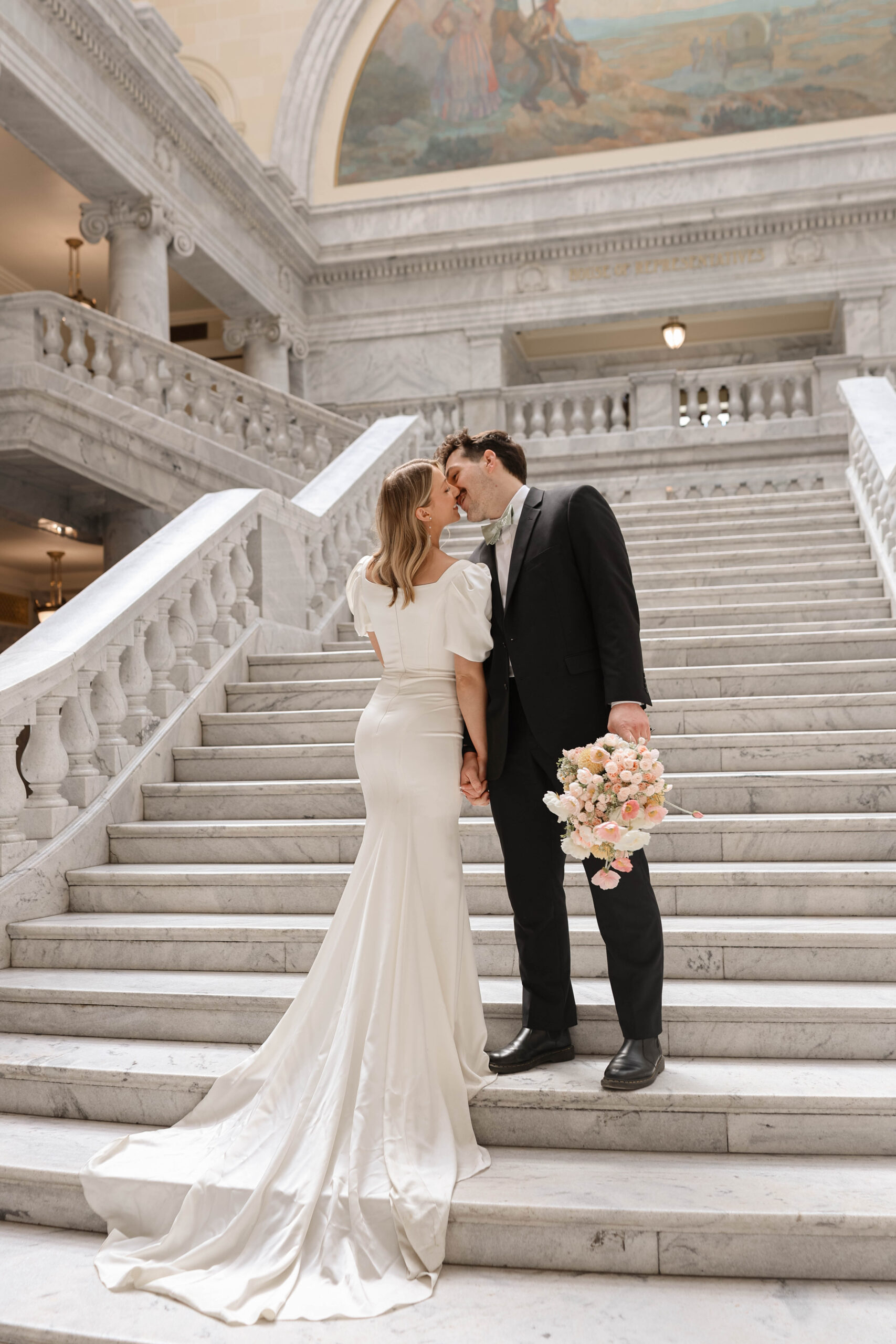 A travel elopement photographer captures a sweet kiss between the bride and groom on the grand staircase of the Utah Capitol building.