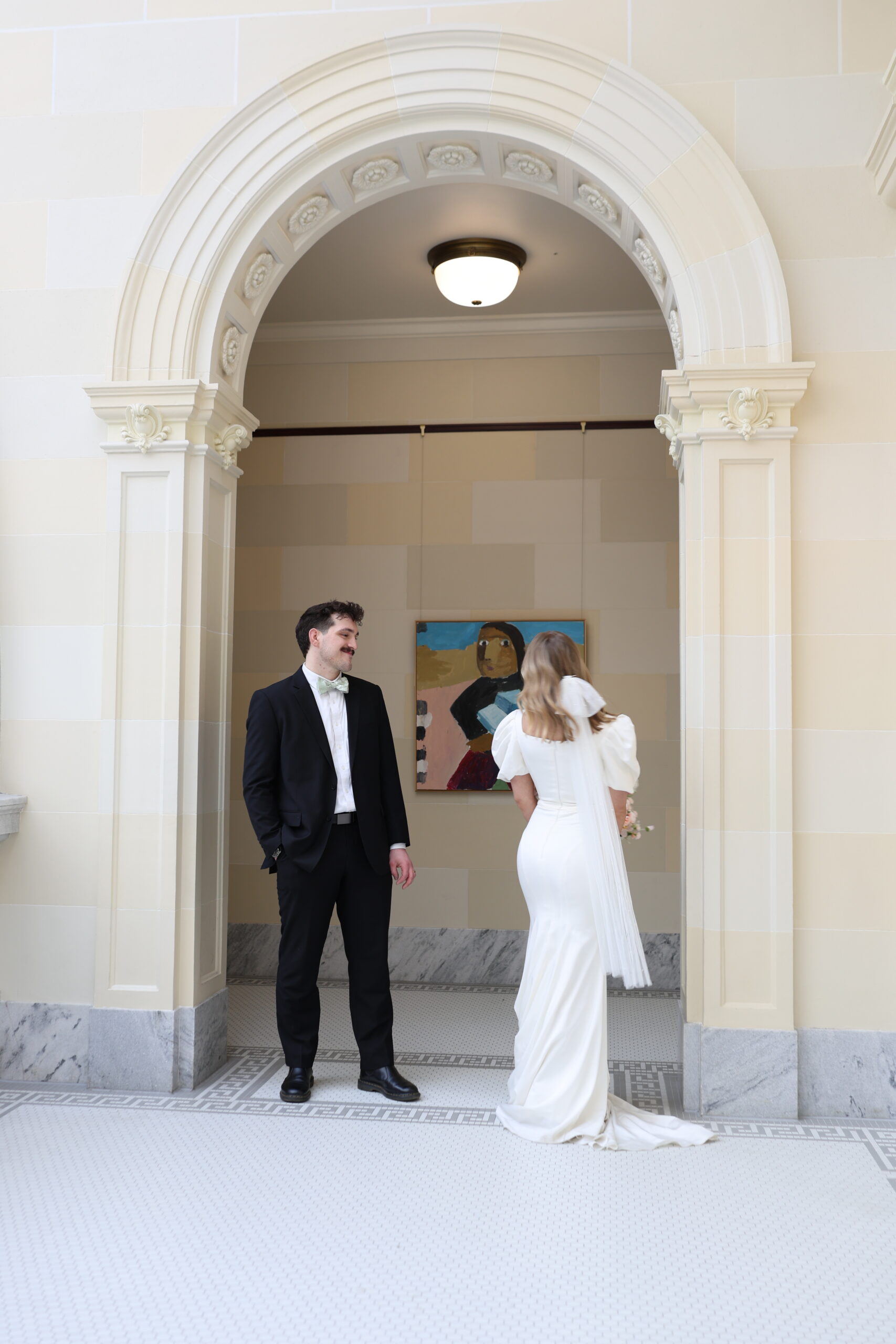 Bride and groom sharing a first look in a marble archway, smiling at each other.