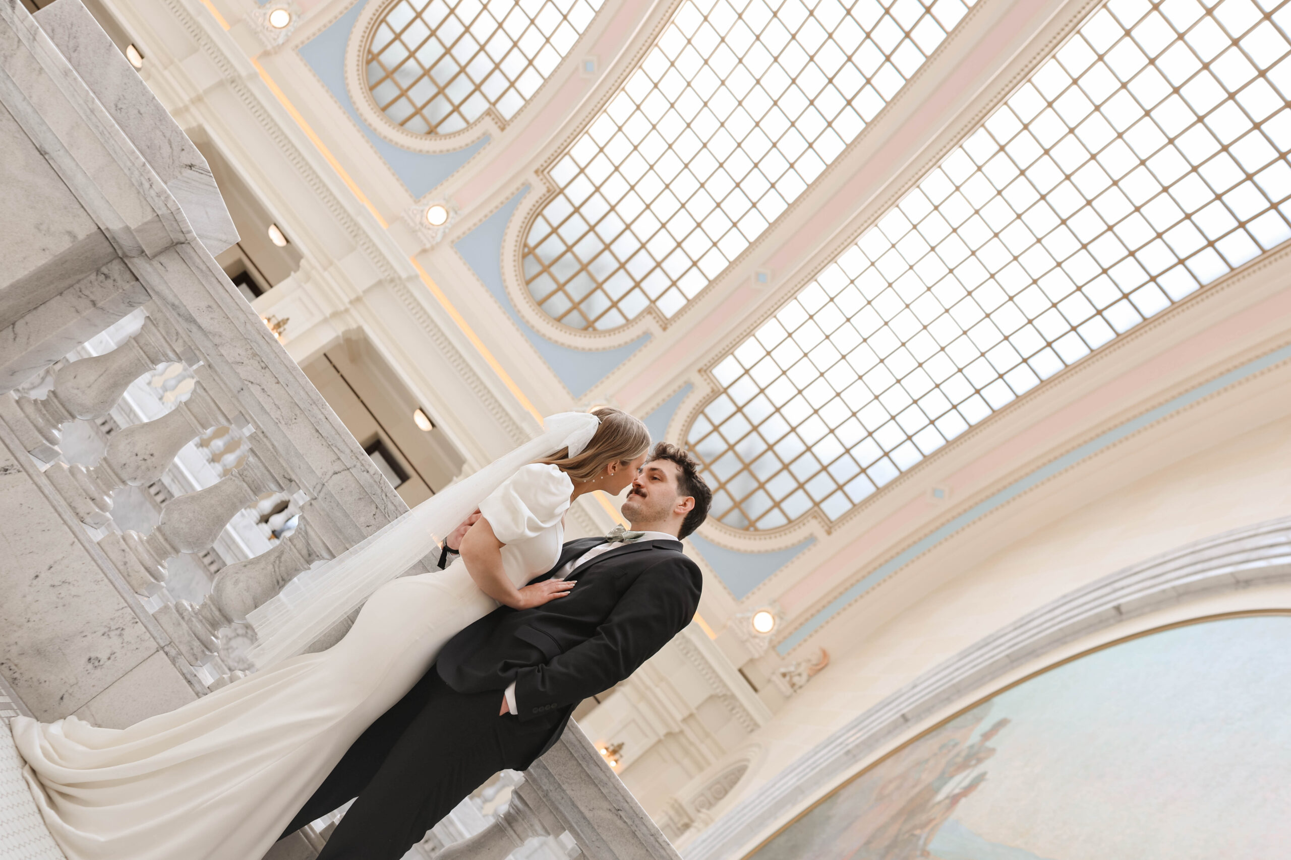An intimate moment captured by a travel elopement photographer as the couple shares a kiss under the curved glass ceiling of a historic venue.