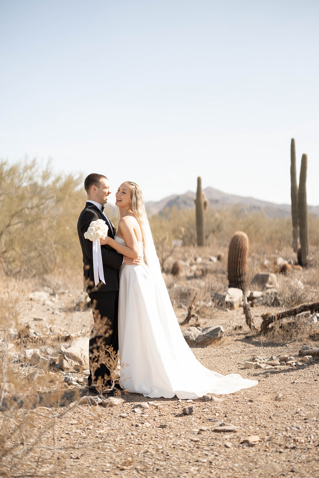The couple smiles and embraces in the middle of the desert, framed by soft golden light and classic Arizona cacti.