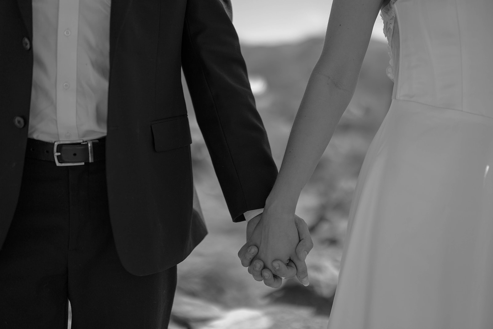 Close-up black and white photo of a bride and groom holding hands during their wedding ceremony.