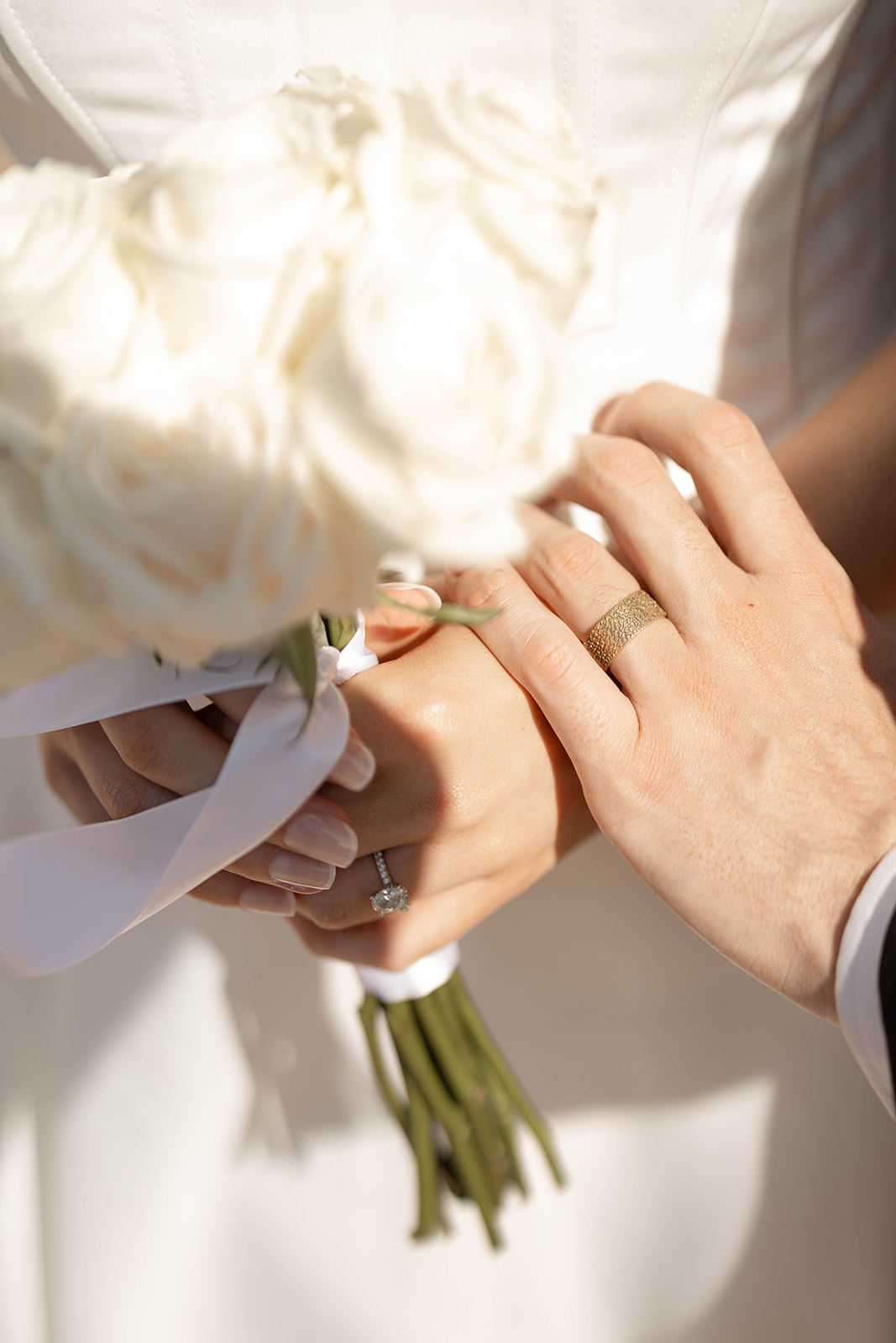 Close-up of hands and wedding rings with the bride holding a white rose bouquet, highlighting the small, meaningful details of the day.
