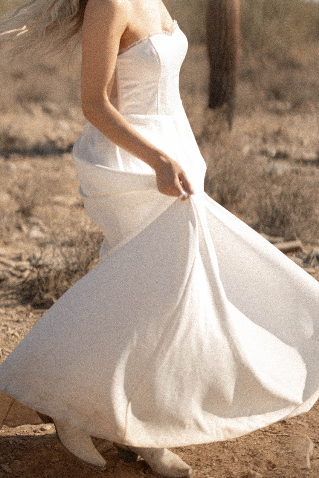 A close-up of a bride's dress flowing as she walks through the desert in white boots, the movement catching the golden desert light.