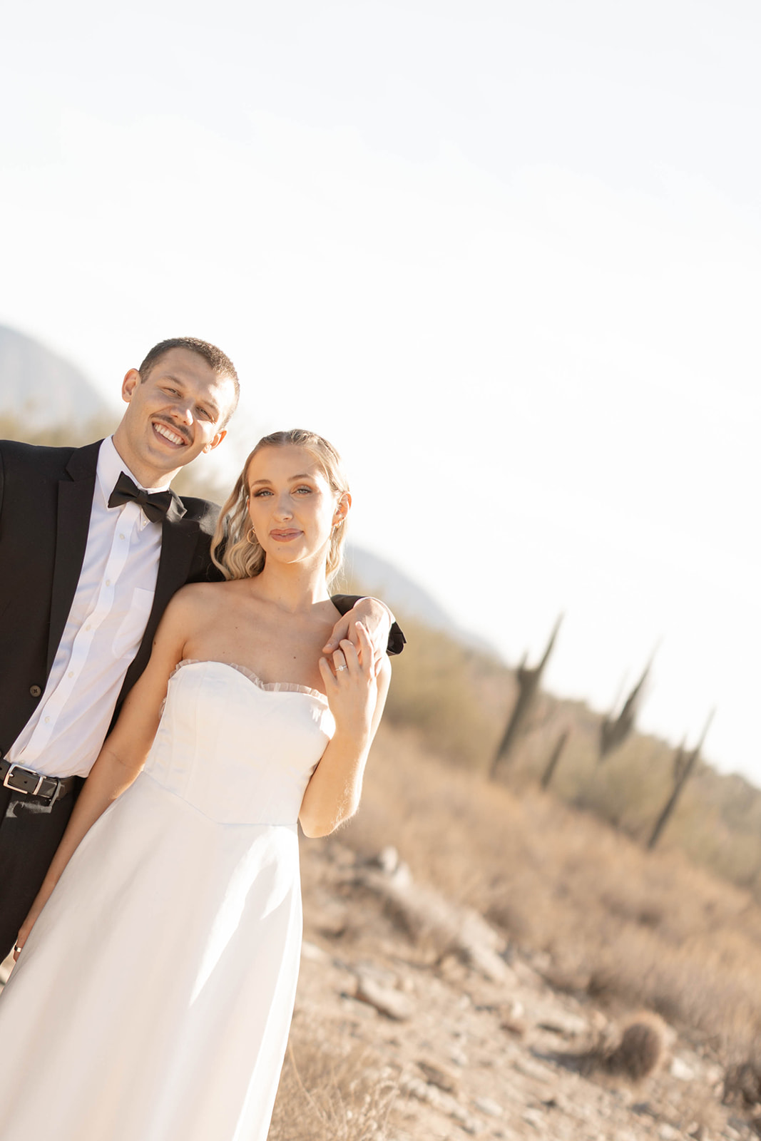 A bride and groom smiling and standing close together in the Arizona desert with cacti in the background, perfect inspiration for couples exploring Arizona elopement locations.