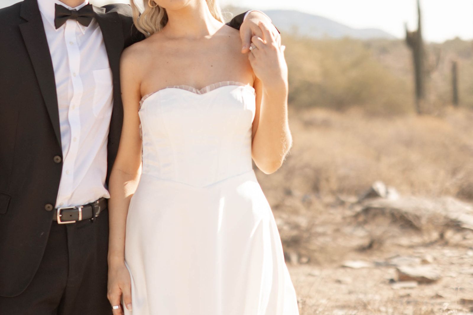 A romantic close-up of the bride’s hand on the groom’s arm, highlighting the soft desert light and elegant wedding attire.
