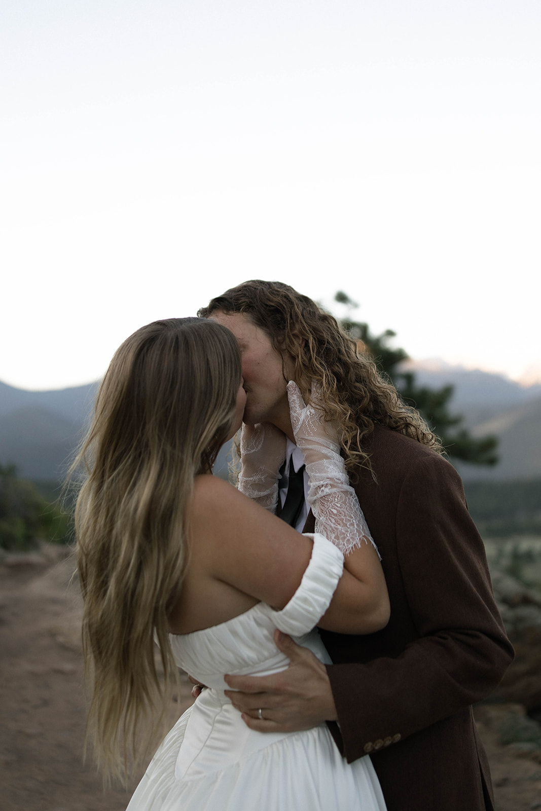A bride and groom share a tender kiss at sunset, surrounded by mountains and trees in one of the most romantic Colorado elopement locations.
