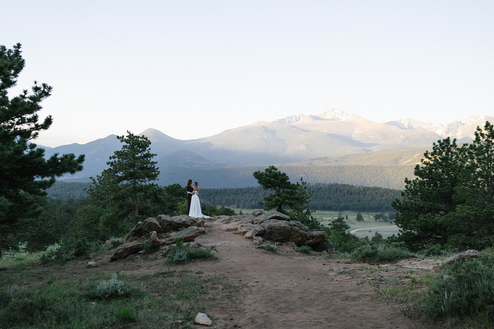 A bride and groom stand together on a rocky overlook with sweeping mountain views in the background, embracing the beauty of Colorado elopement locations.