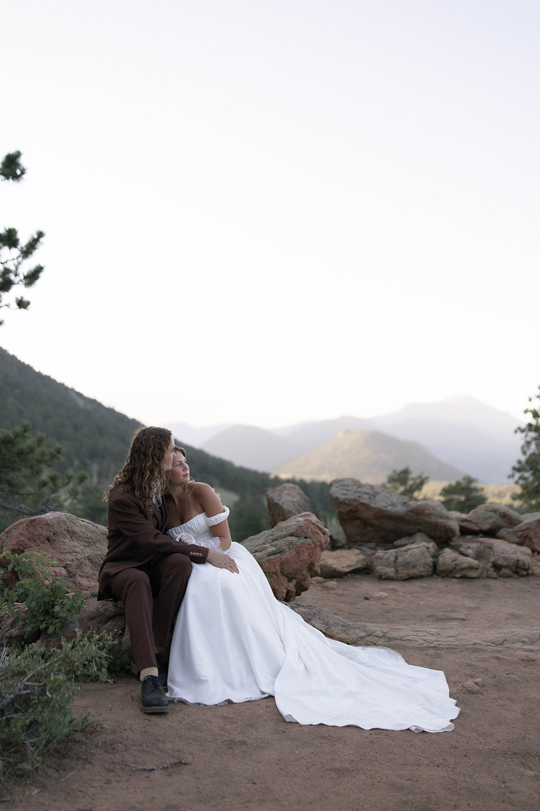 The couple sits nestled among rocky terrain, gazing off into the distance as layers of Colorado mountains stretch behind them—one of the most peaceful Colorado elopement locations.