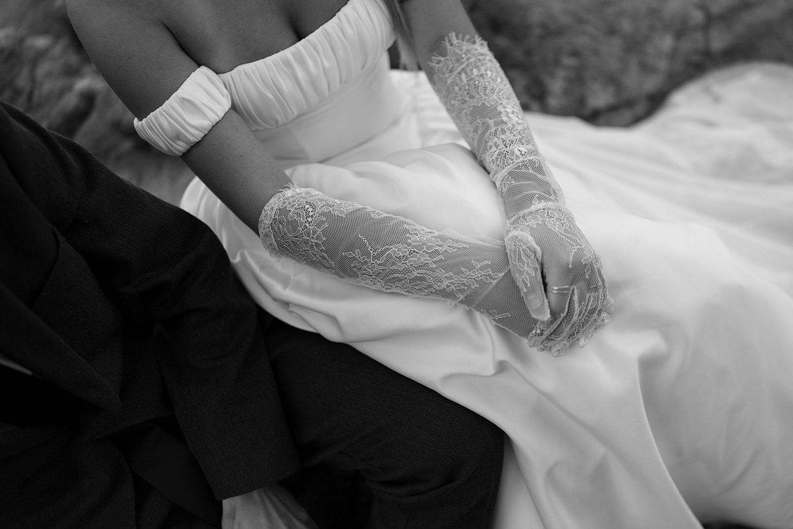 A black and white close-up of a bride’s lace gloves resting gently on her lap, capturing a quiet and intimate detail from the ceremony.