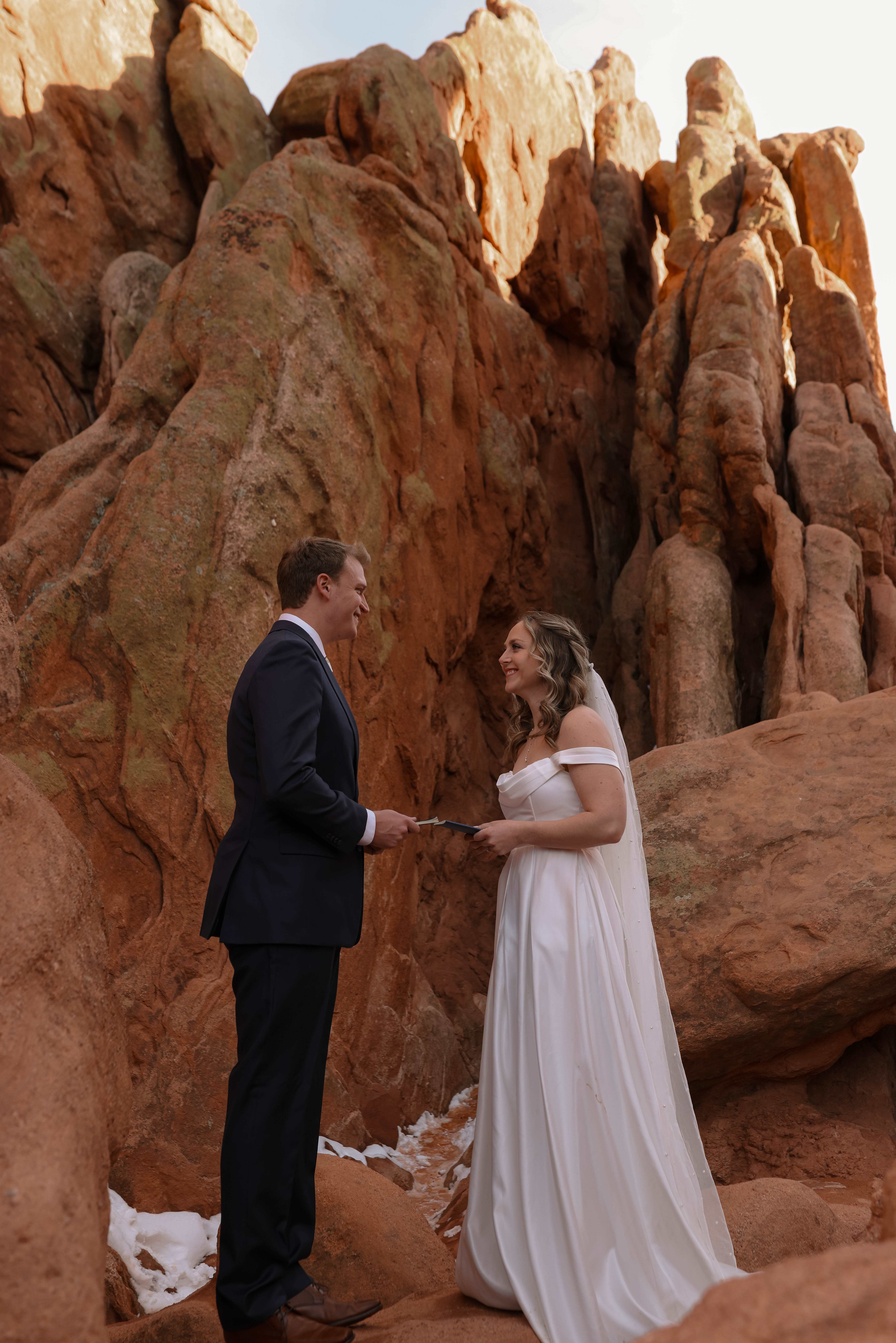 A couple stands before the dramatic textures of red rocks, holding their vows and sharing a quiet moment during their elopement.