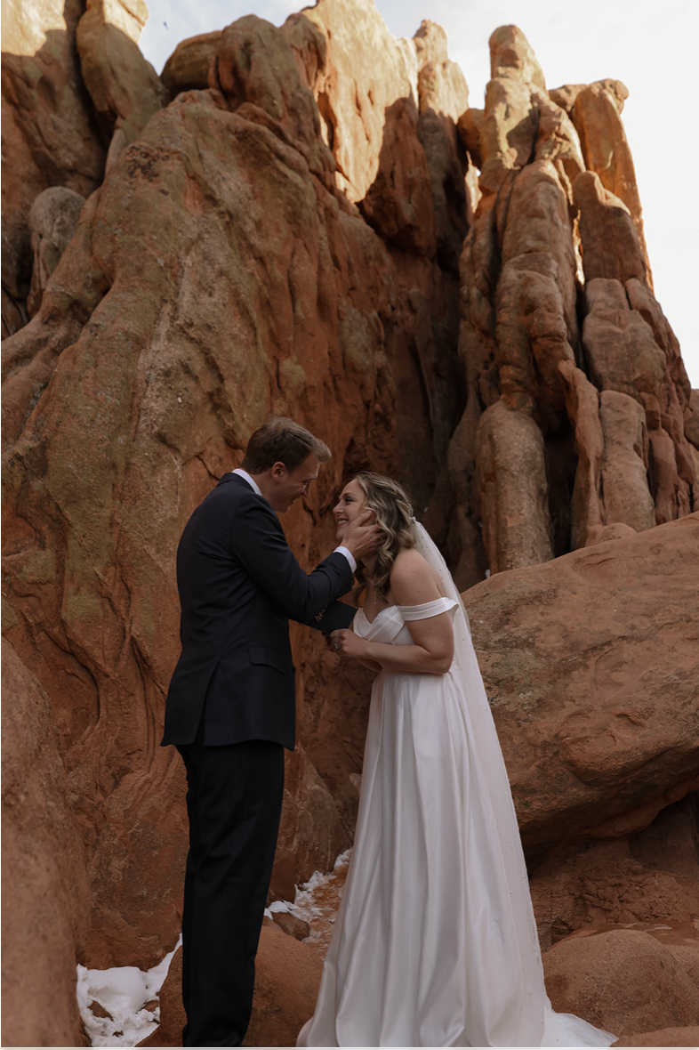 A sweet moment as the groom cradles the bride’s face while standing among the dramatic red rocks of Garden of the Gods—capturing the magic of an intimate Colorado elopement.