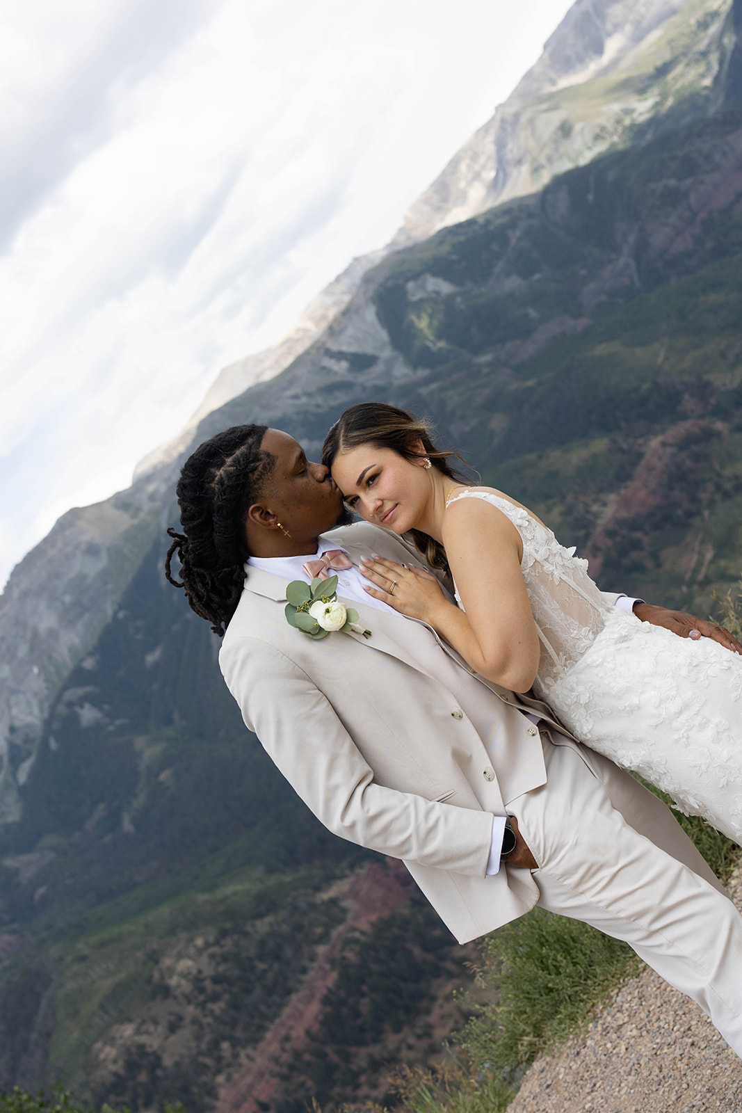 Groom kisses bride’s forehead as they embrace against the dramatic mountain backdrop during their Telluride elopement.