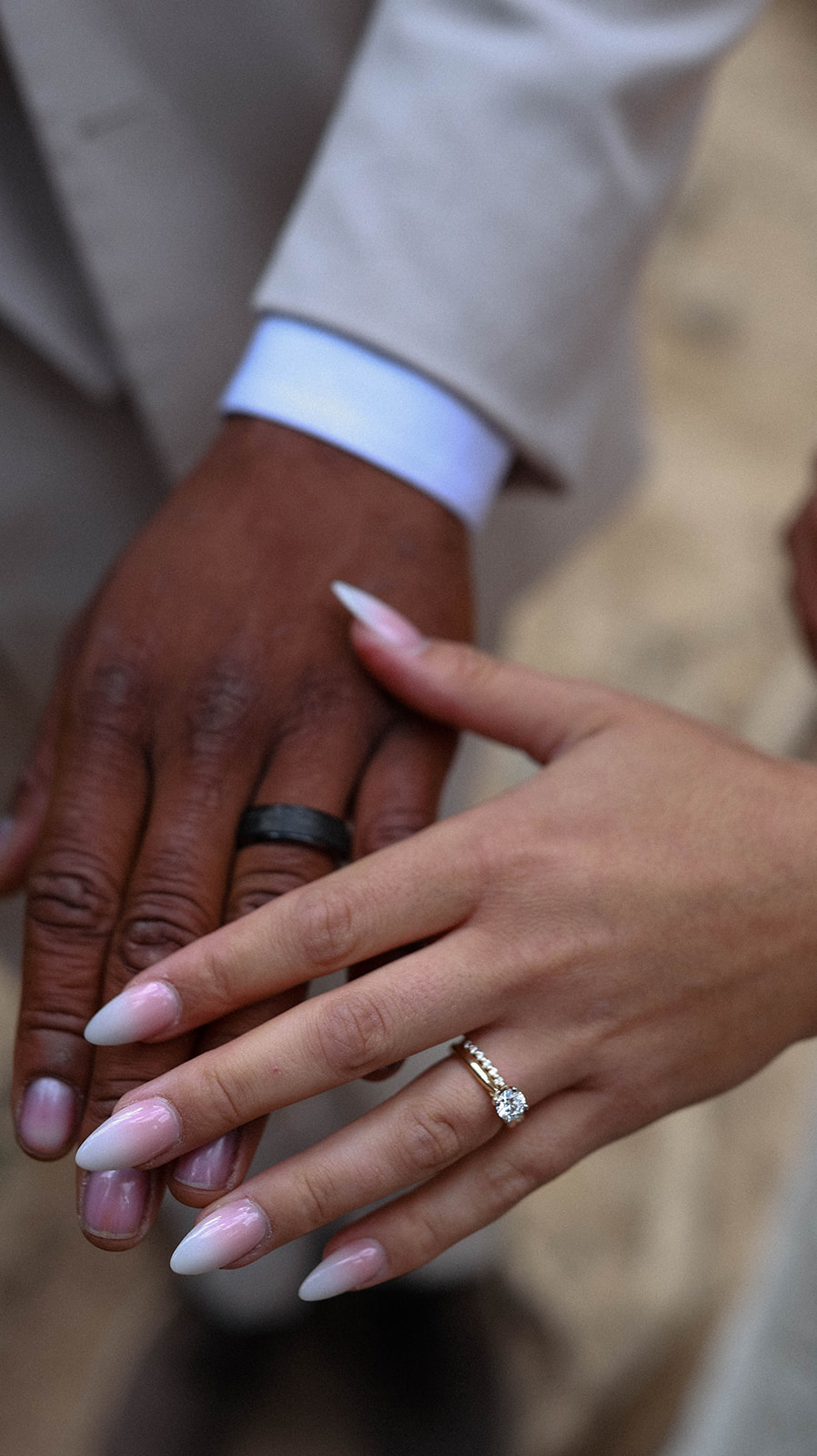Close-up of intertwined hands showing wedding rings, the bride’s diamond engagement ring gleaming in soft light.