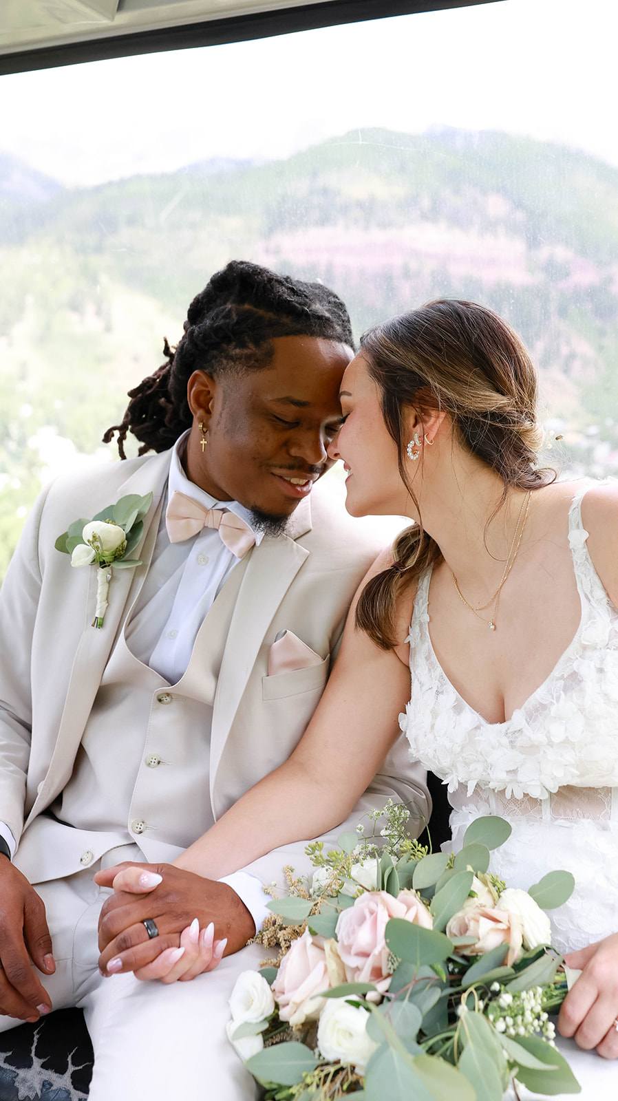 Bride and groom leaning their foreheads together, smiling softly while holding a bouquet of blush and ivory flowers.