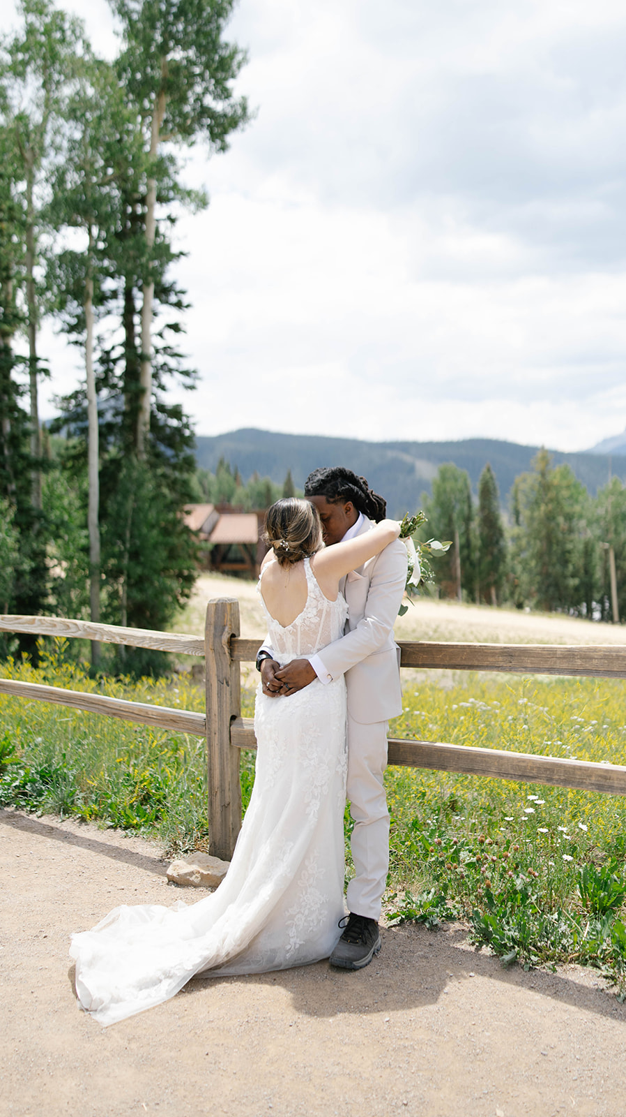 Bride and groom share a kiss by a wooden fence with wildflowers and mountains in the background during their Telluride elopement.