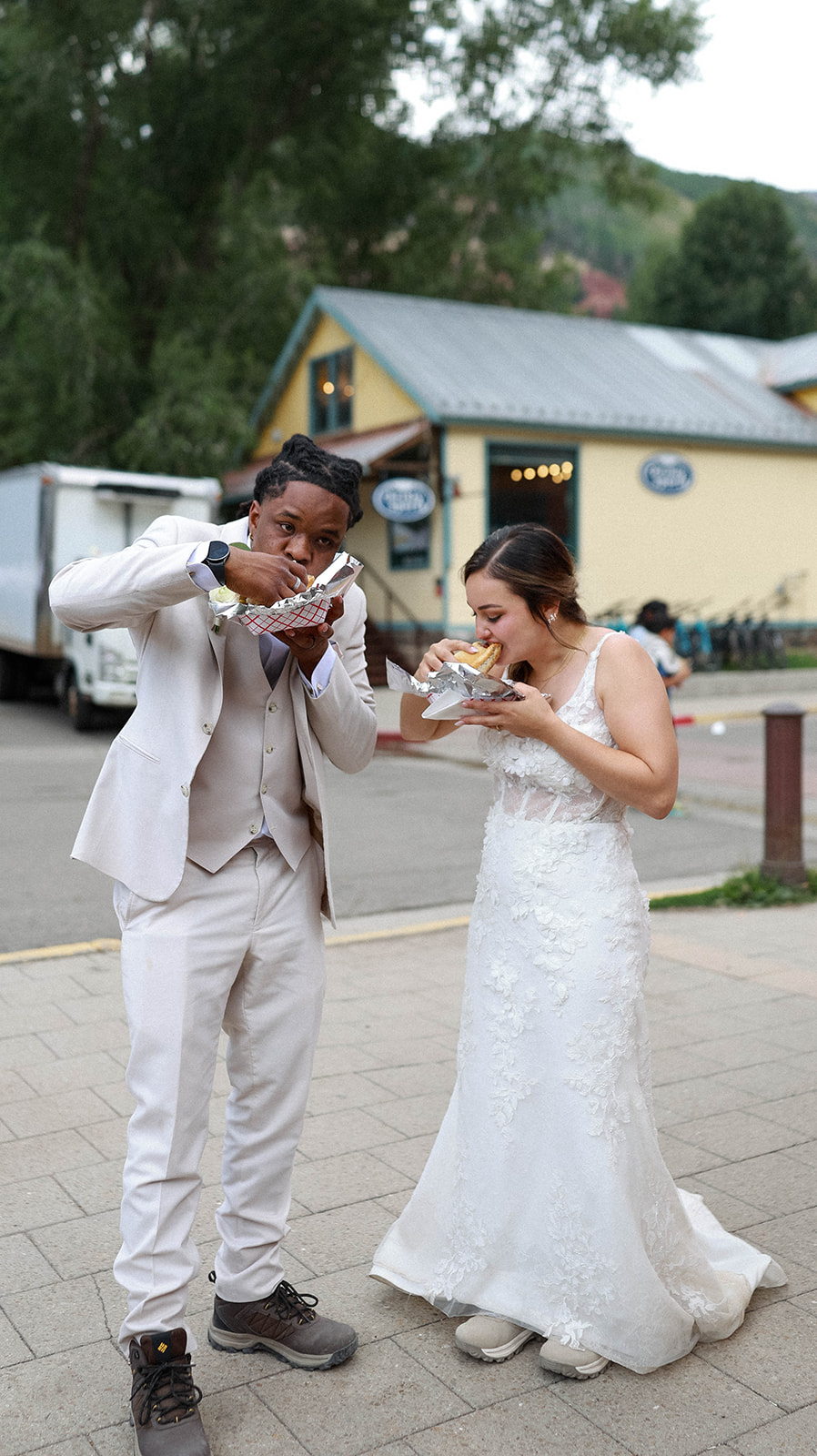 Newlyweds share a fun moment eating street food in their wedding attire after their Telluride elopement.