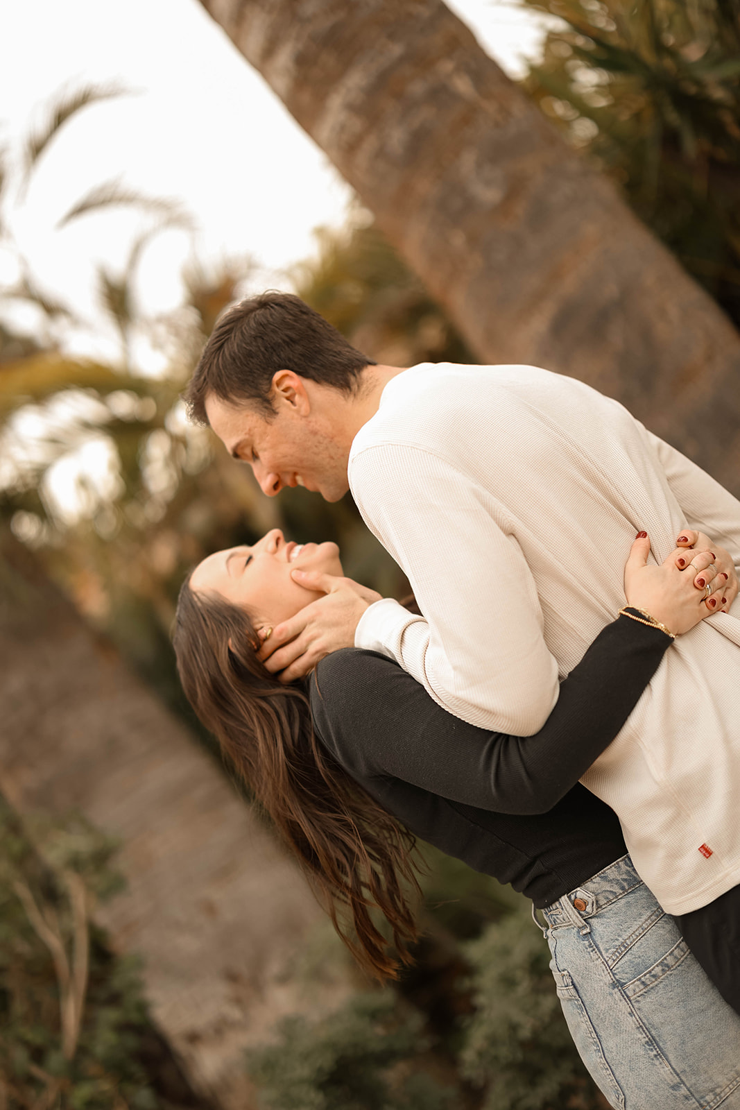 Romantic couples photos by a tall cactus with the couple leaning into each other and smiling softly.