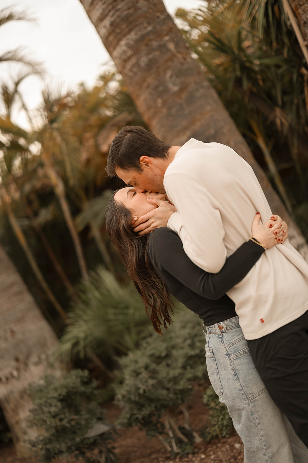 Couples photos of an intimate kiss as the man leans down and the woman holds his face, surrounded by tropical greenery.