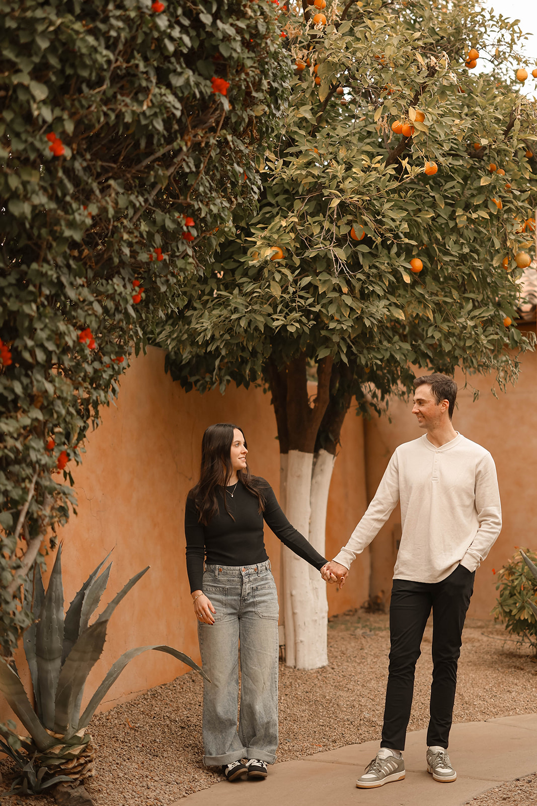 Couple walking together hand in hand beneath an orange tree in a garden courtyard.