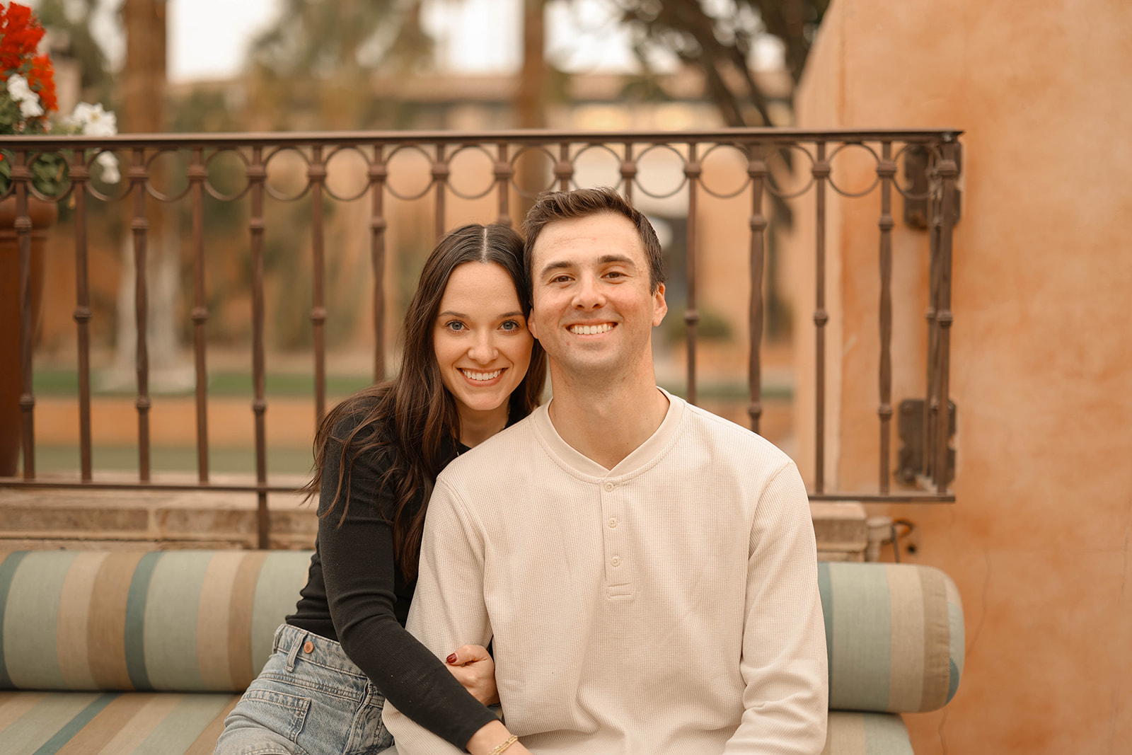 A warm portrait of a couple sitting on a striped bench, smiling directly at the camera.