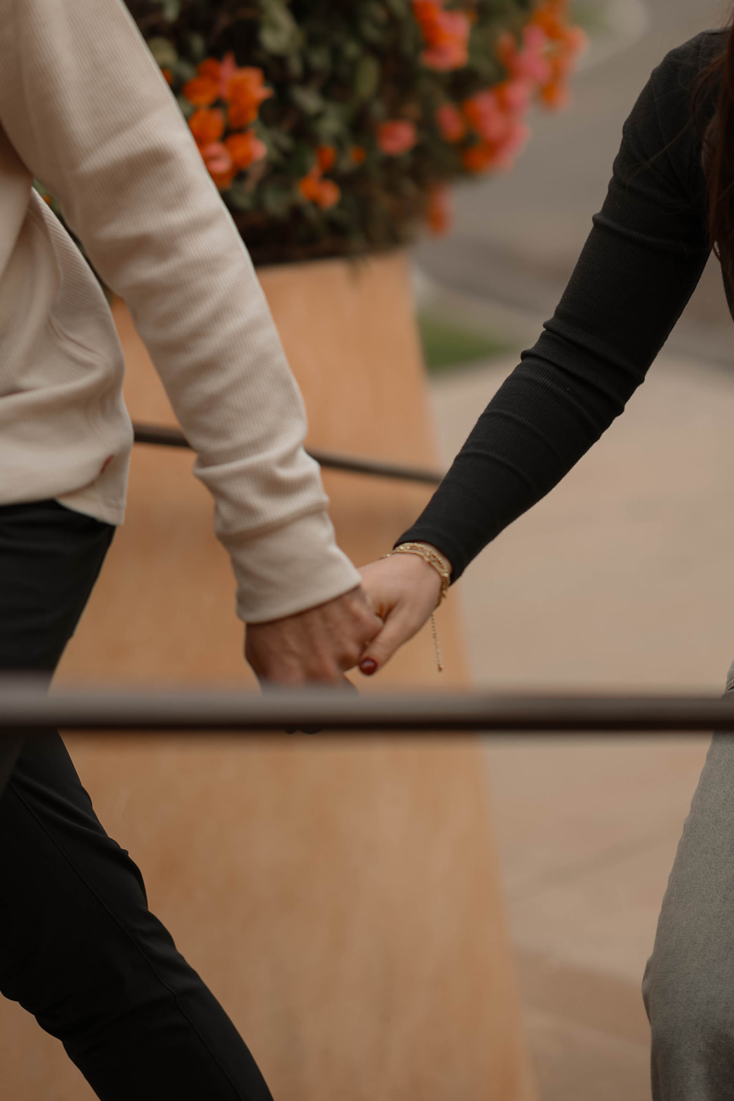 Close-up couples photos of hands intertwined against orange flowers and adobe tones.
