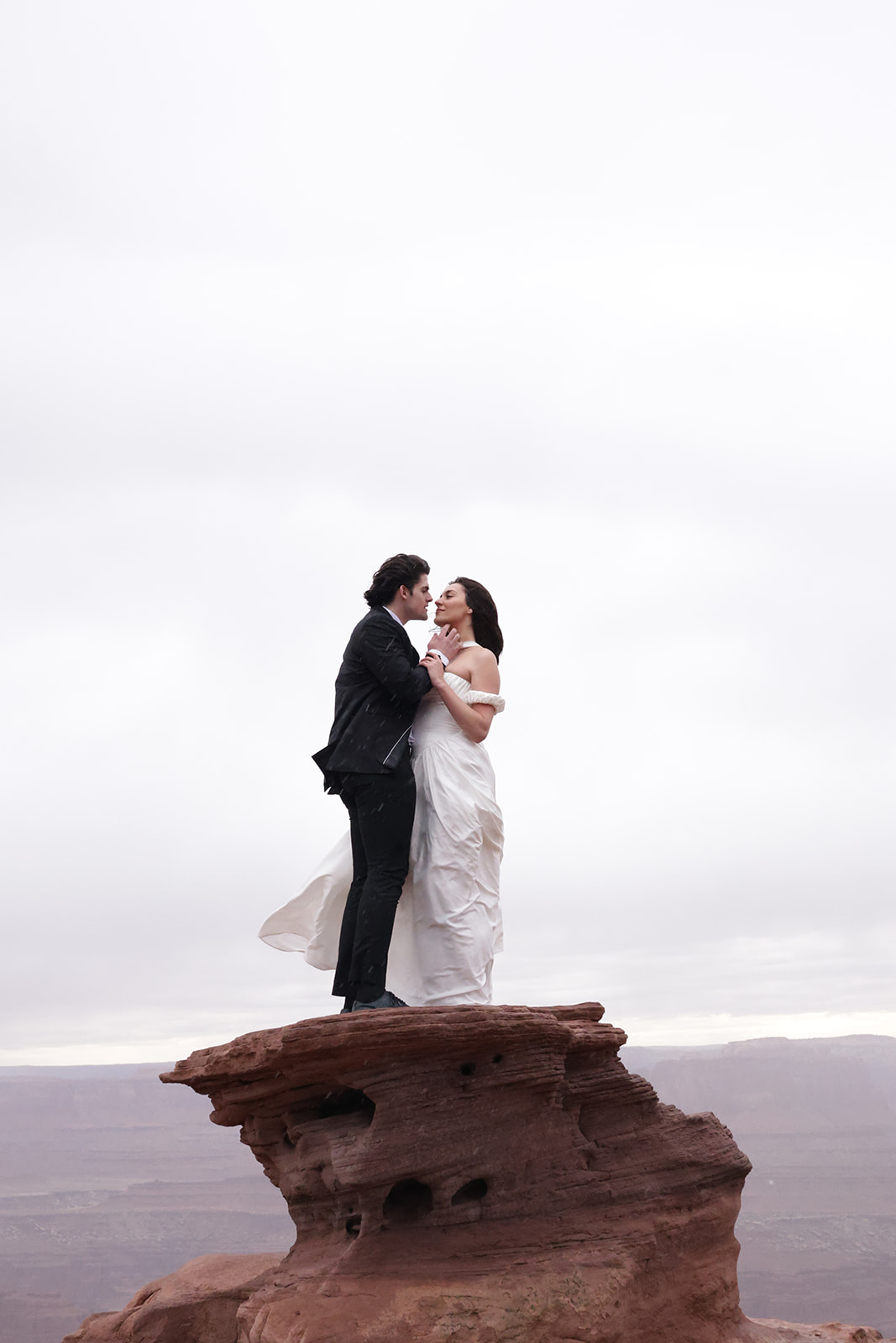Romantic desert scene with bride in a simple, elegant elopement outfit and groom gazing lovingly at each other.