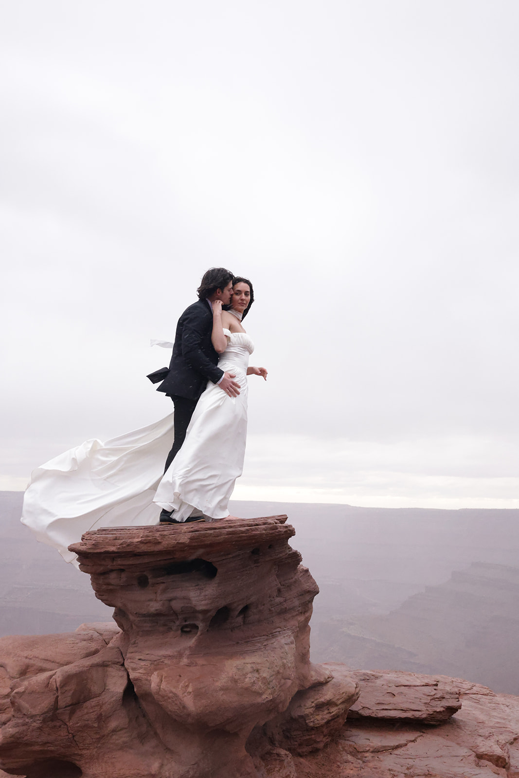 Bride and groom standing on red rock overlooking desert landscape, captured during a moody elopement session.