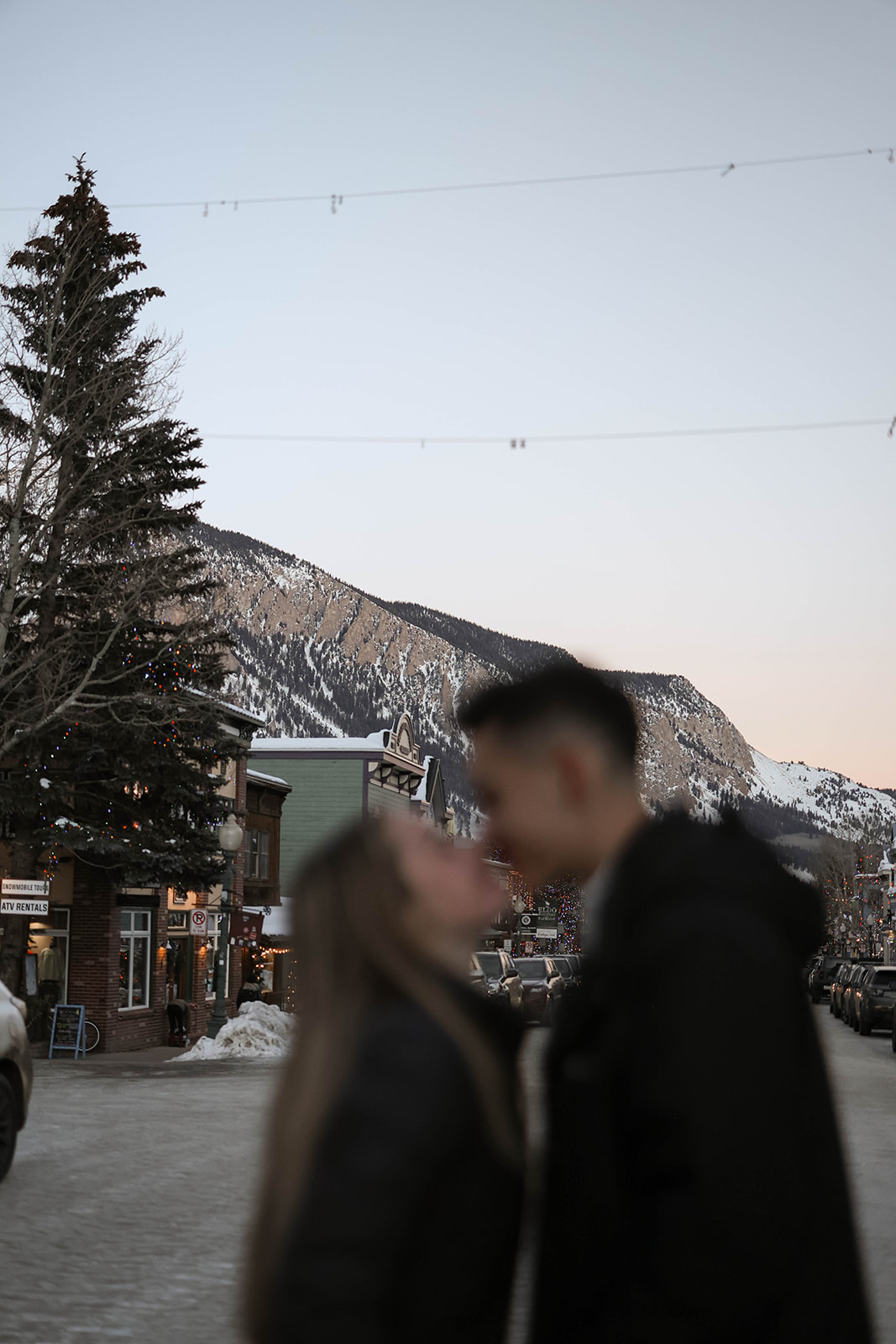 Out-of-focus couple sharing a kiss on a wintery street with a mountain backdrop.