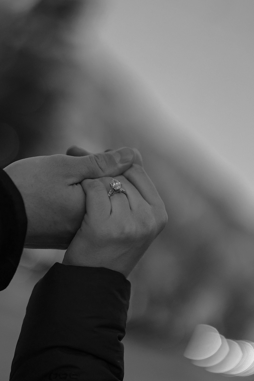 Black-and-white close-up of hands clasped together, showing an engagement ring — surprise proposal detail.