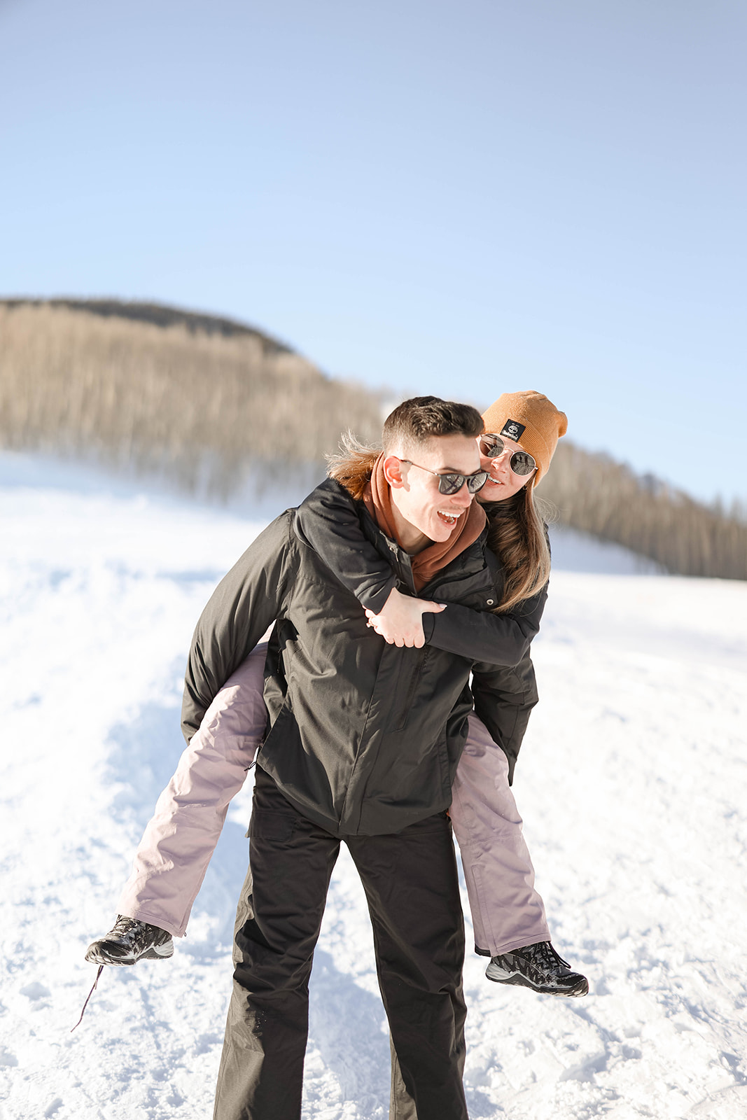 Playful piggyback ride in the snow, both smiling under the bright winter sun.