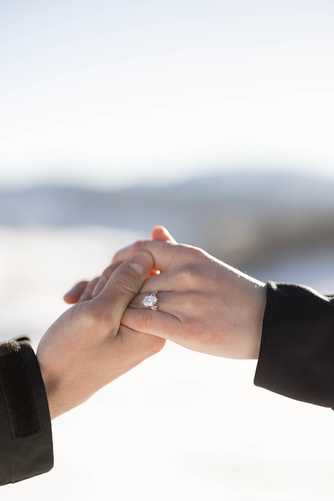 Close-up of hands clasped together, showcasing a sparkling engagement ring from a surprise proposal.