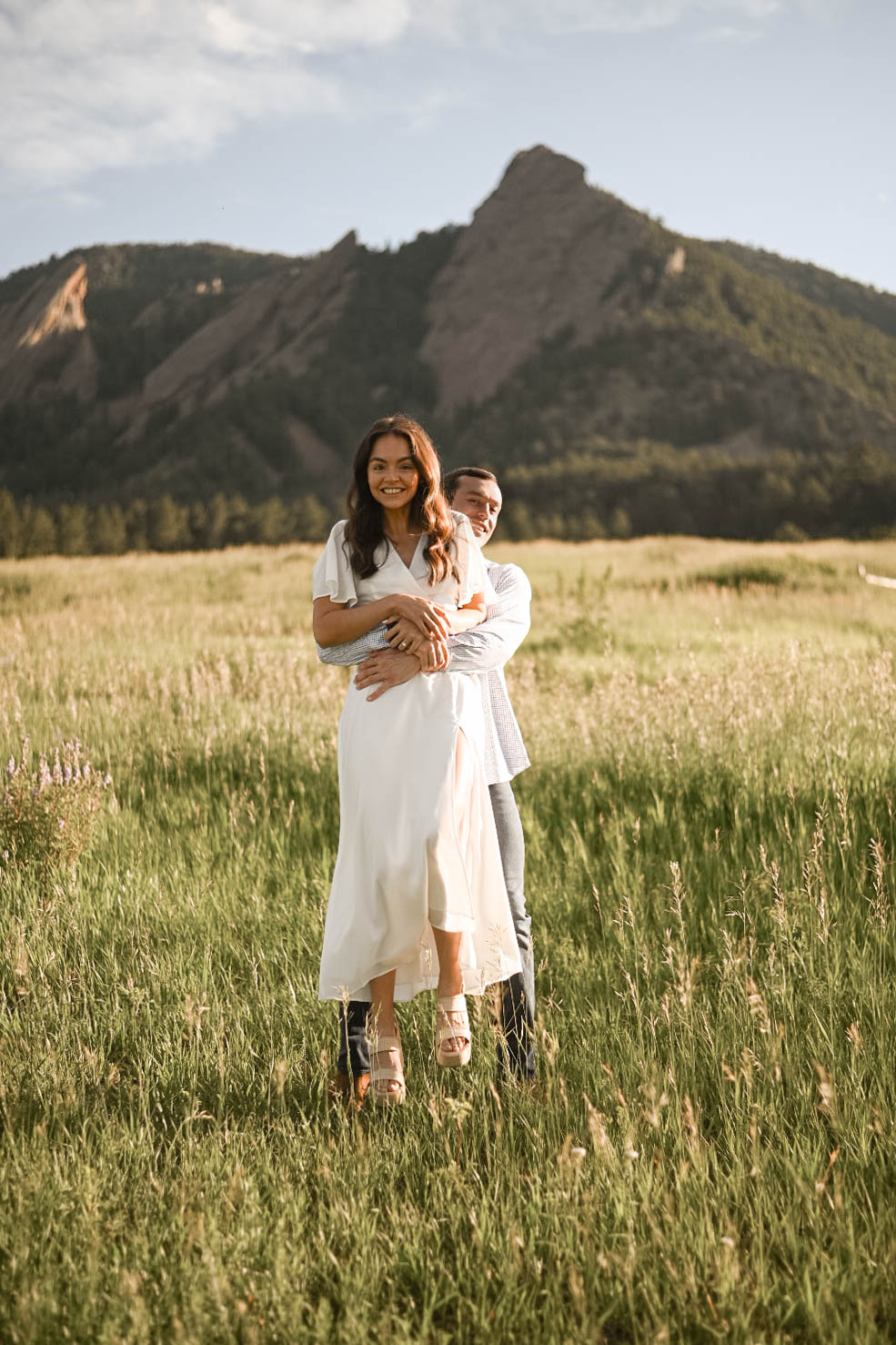 Man lifting his fiancée playfully in a field with the iconic Flatirons of Chautauqua Park, Boulder behind them.