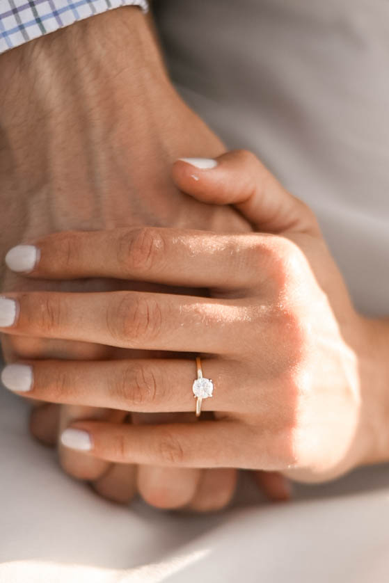 Detail shot of a bride-to-be’s hand wearing a solitaire engagement ring while holding her partner’s hand