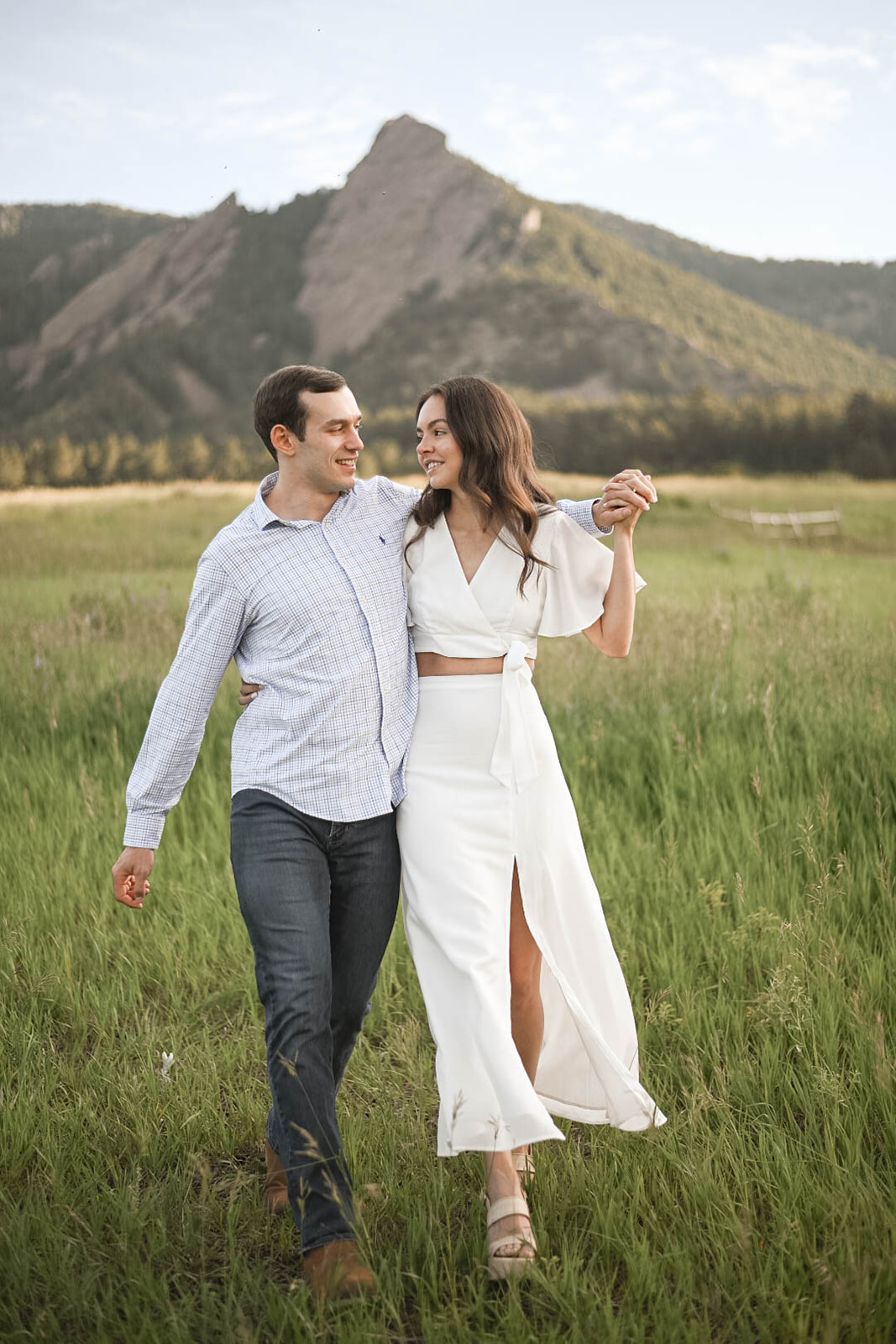 Couple holding hands and walking together through an open meadow at Chautauqua Park, Boulder.