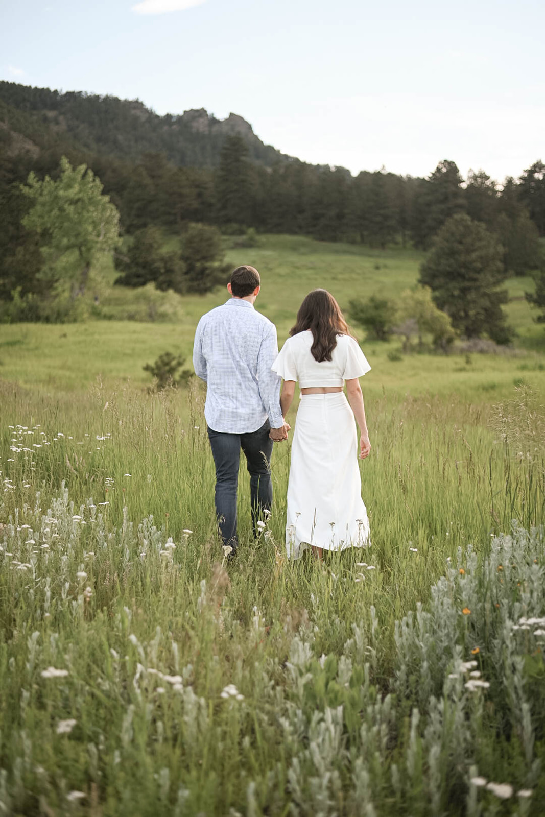 Couple walking away hand in hand through a wildflower-filled meadow at Chautauqua Park, Boulder, surrounded by mountains.