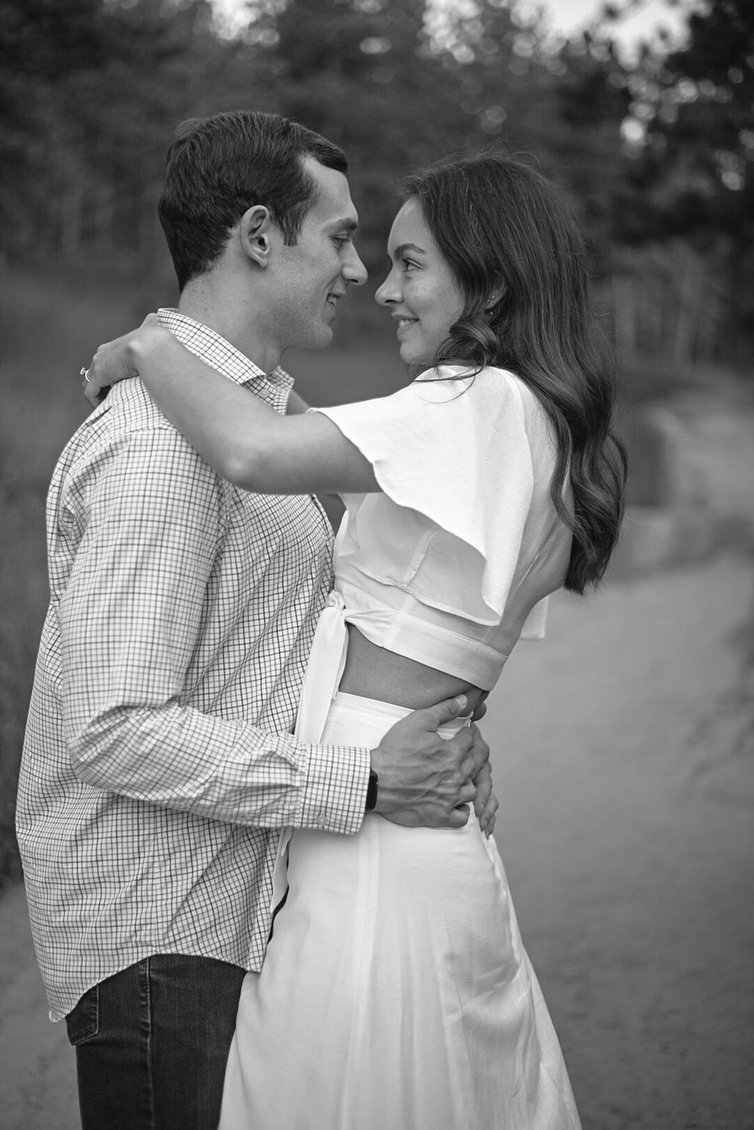 Black and white photo of a couple embracing on a trail, looking into each other’s eyes.