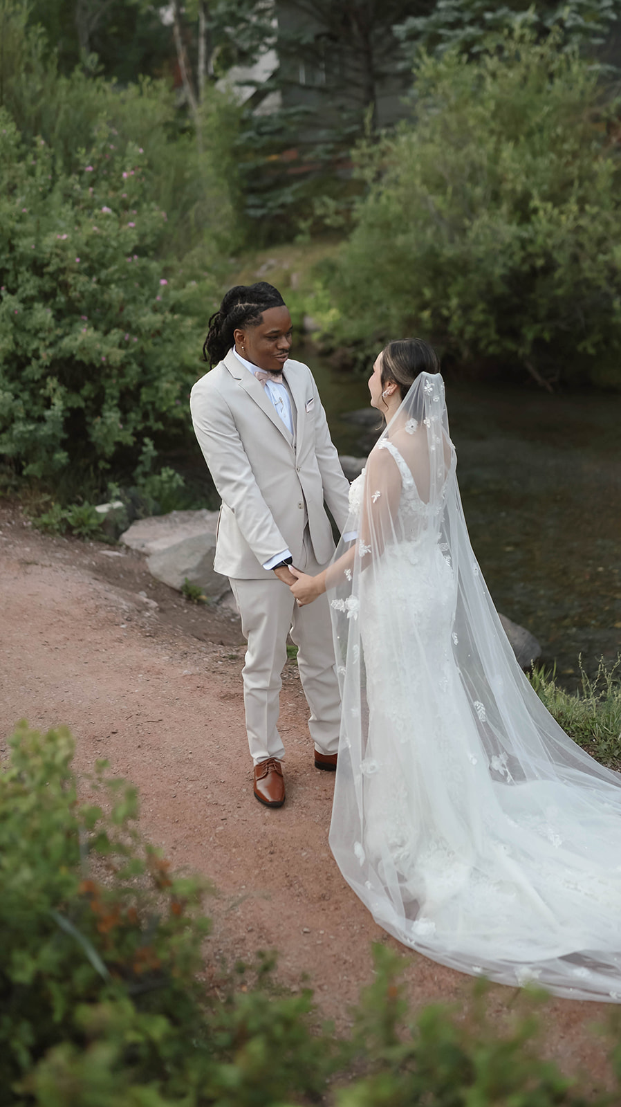 Bride and groom holding hands during their first look by a creek, captured by a colorado elopement photographer.