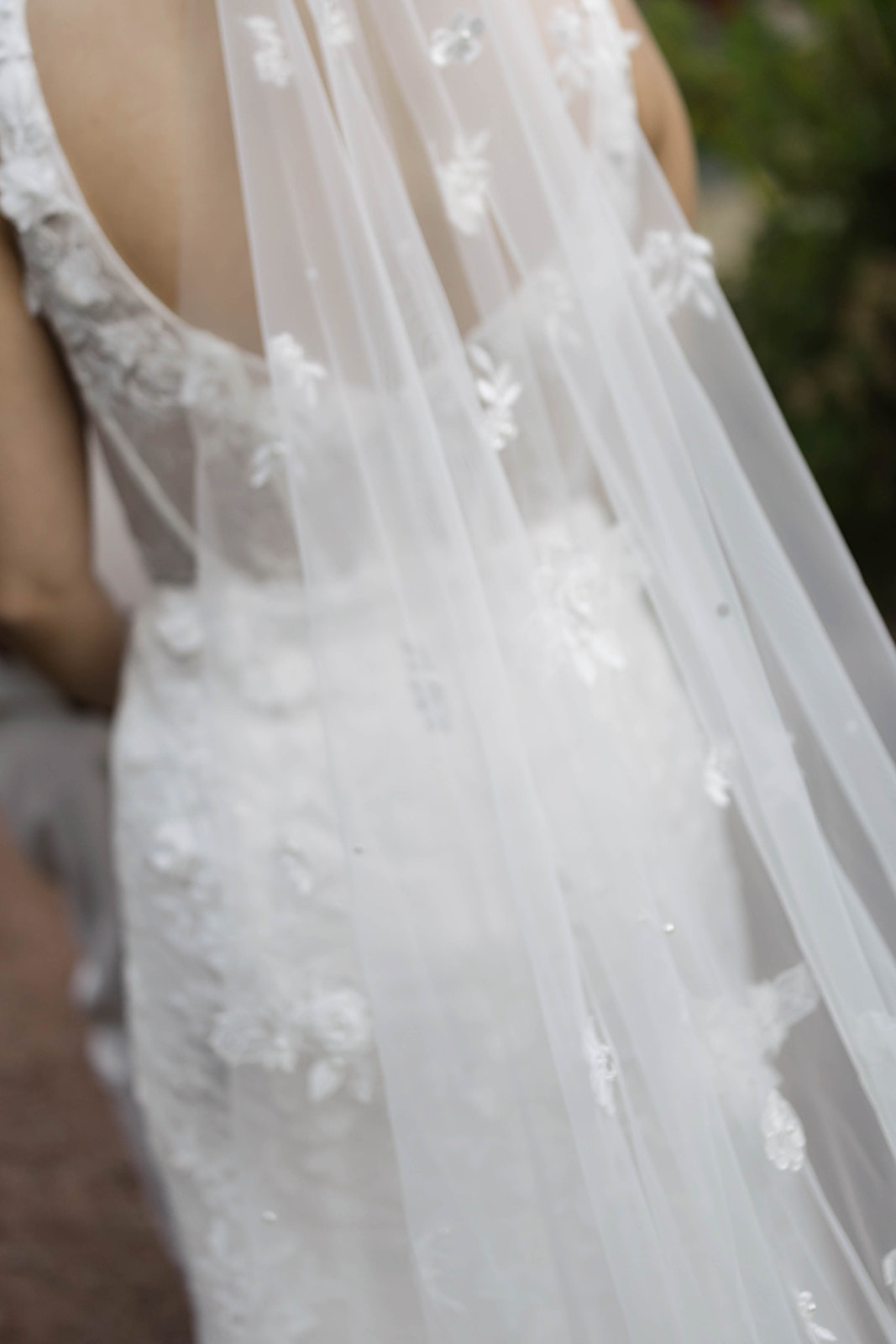 Close-up of the bride’s lace wedding gown and embroidered veil flowing down her back.