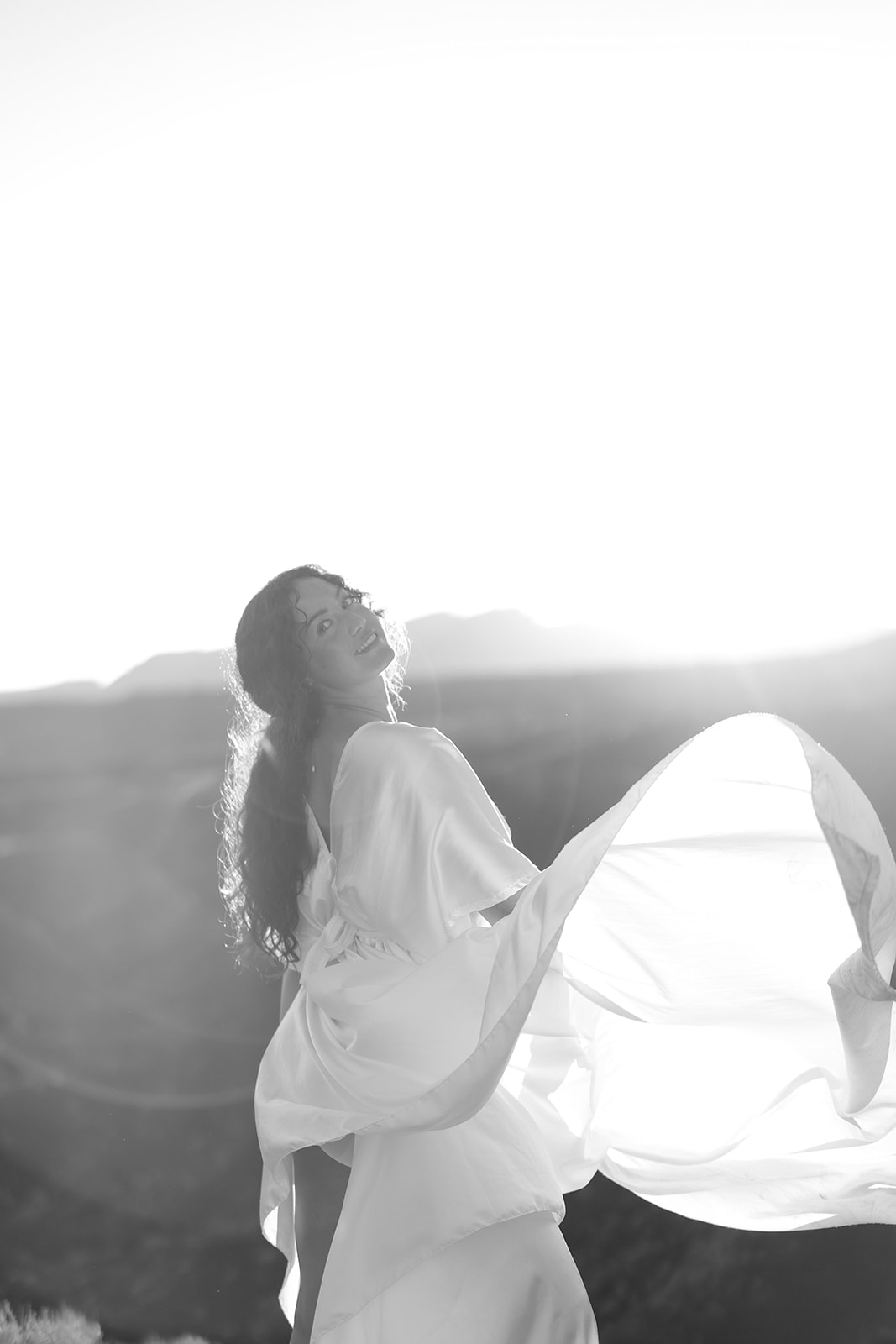 Black and white photo of a bride twirling her flowing silk gown in the desert sunlight, hair loose and windswept.