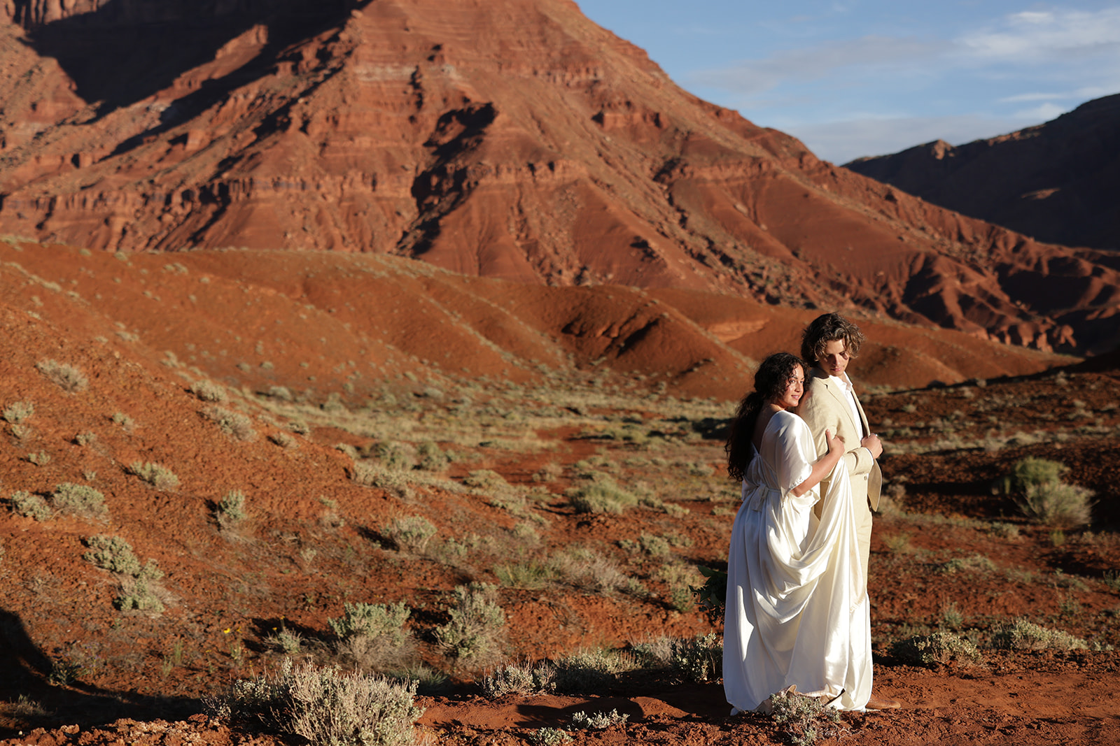 Romantic portrait of a couple standing together with a desert mesa in the background, in Castle Valley, Utah.