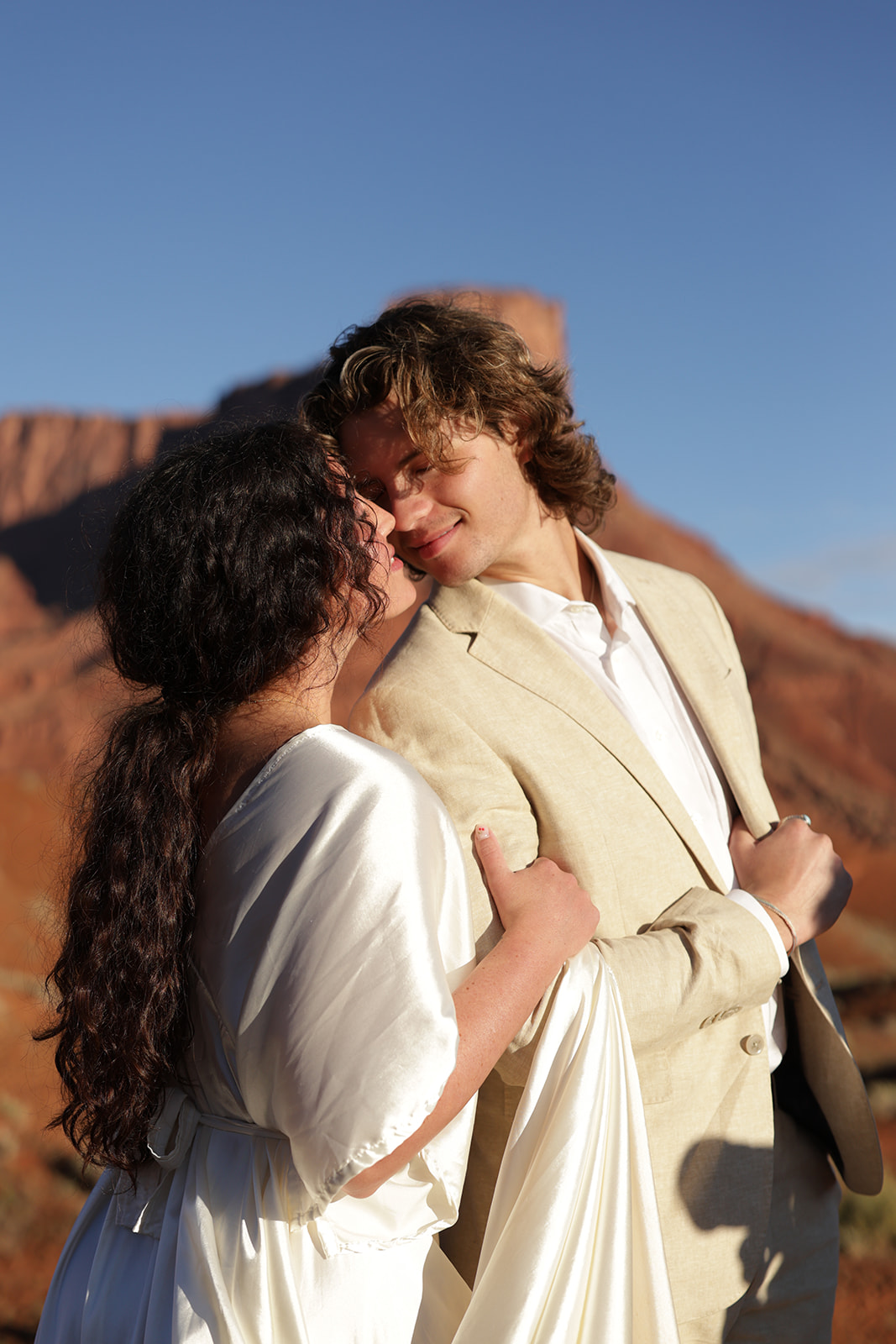 Bride and groom share an intimate moment with the red rock mesas behind them, showcasing the beauty of Castle Valley, Utah.