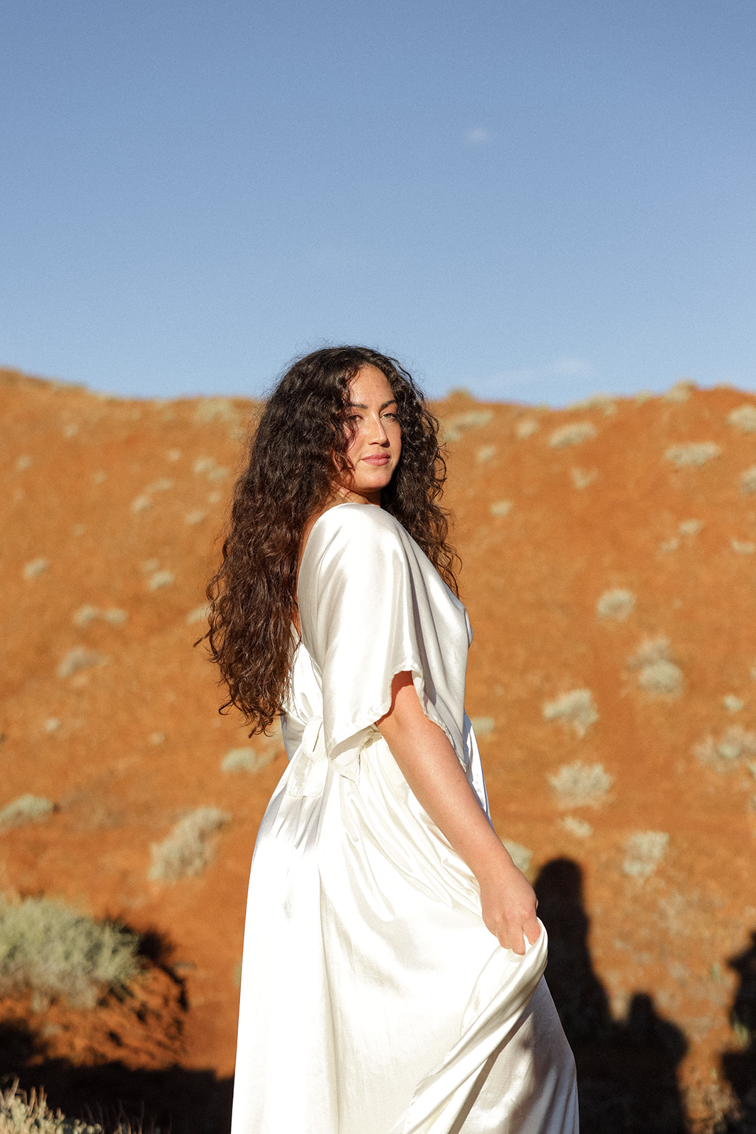 Bride looks back toward the camera with her long curls flowing, warm desert tones all around her.