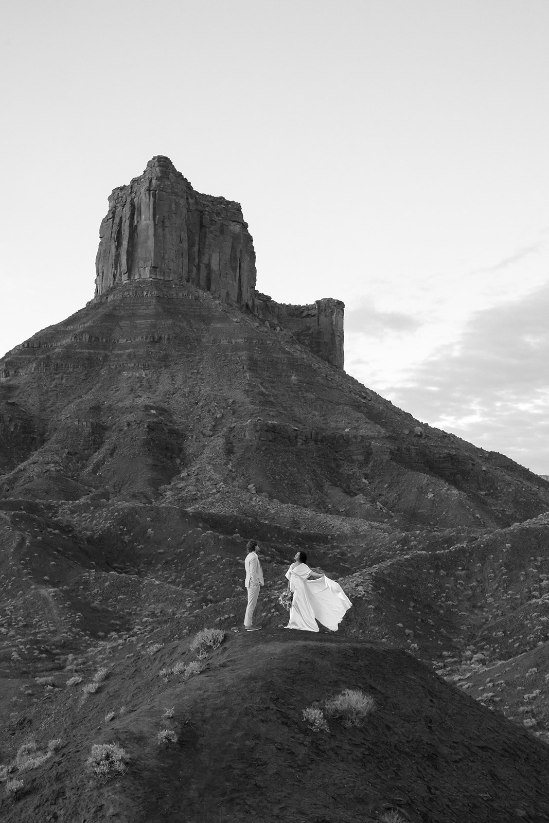 Bride and groom stand together at the base of a dramatic desert rock formation, highlighting the natural beauty of Castle Valley, Utah.