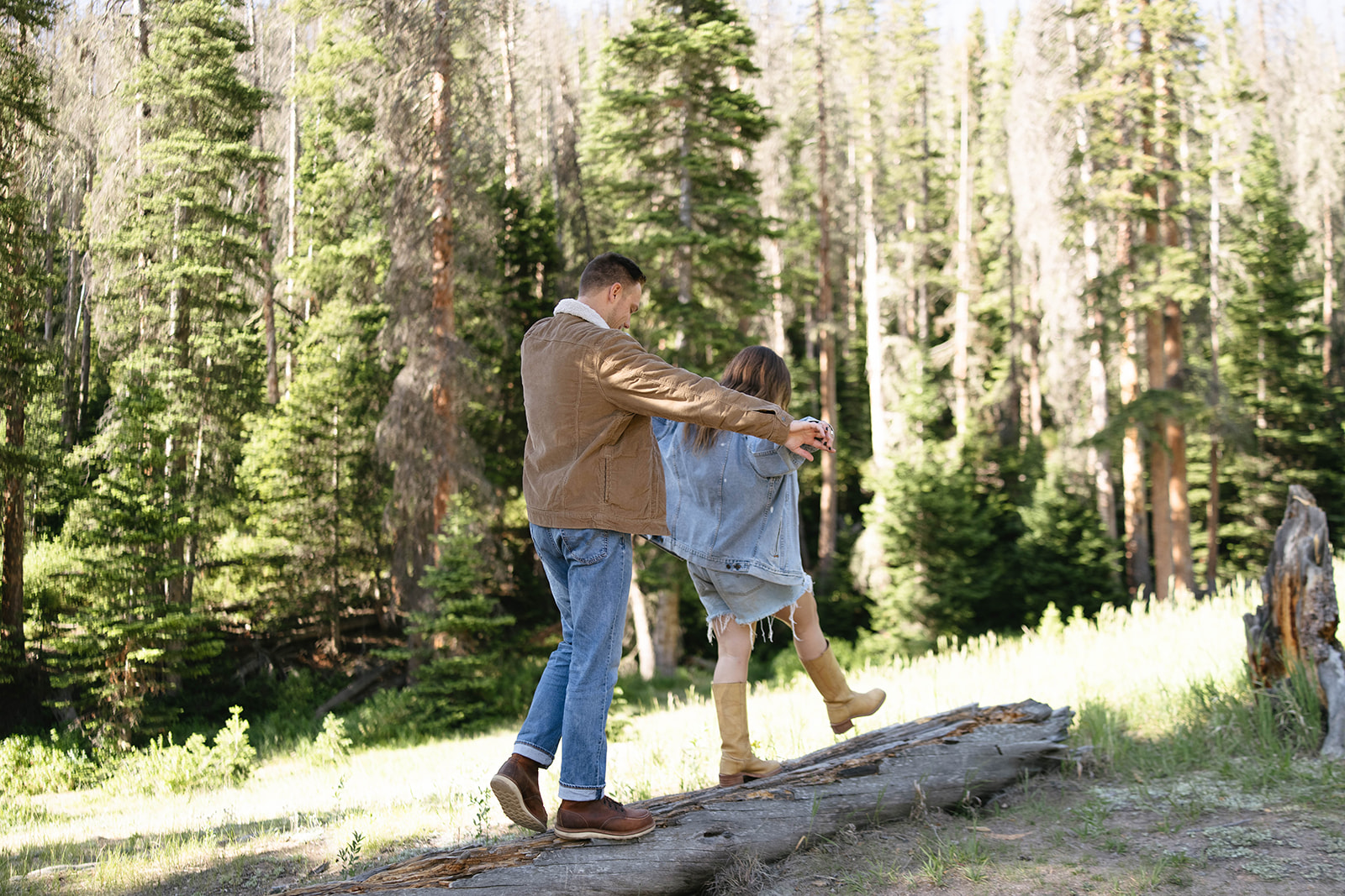 A couple balancing on a log together in the woods, holding hands as they walk through a playful mountain wedding-inspired adventure.