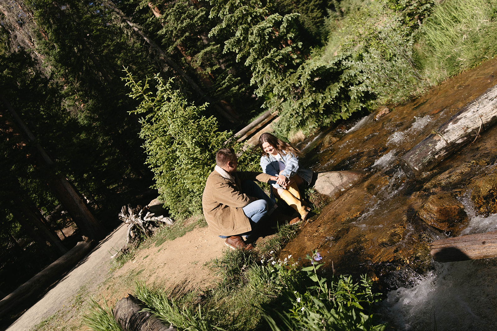 Intimate photo of a couple sitting by a stream, laughing together with the sound of running water in the background.