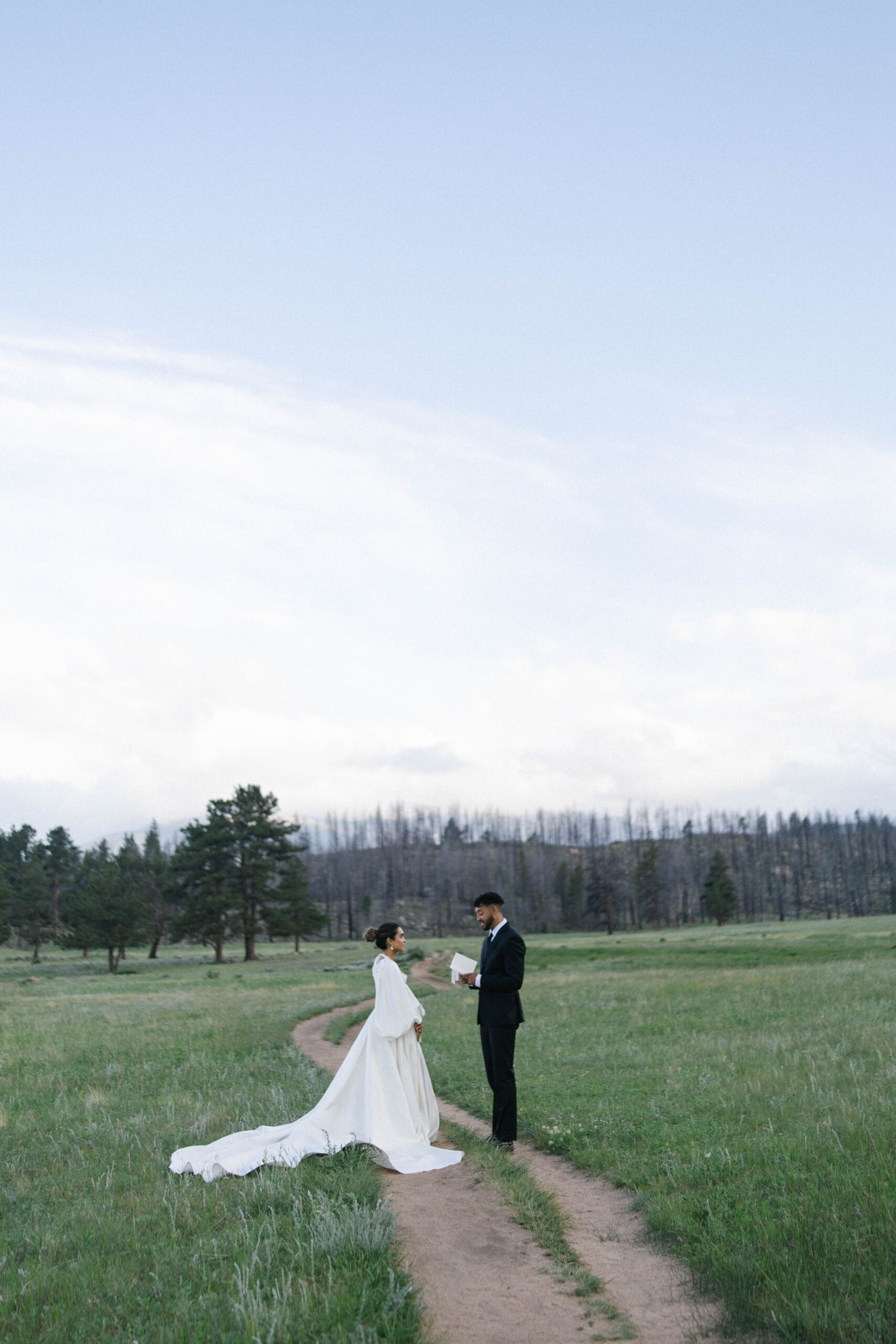 Bride and groom exchanging vows on a trail with mountain views in the distance during their mountain wedding.