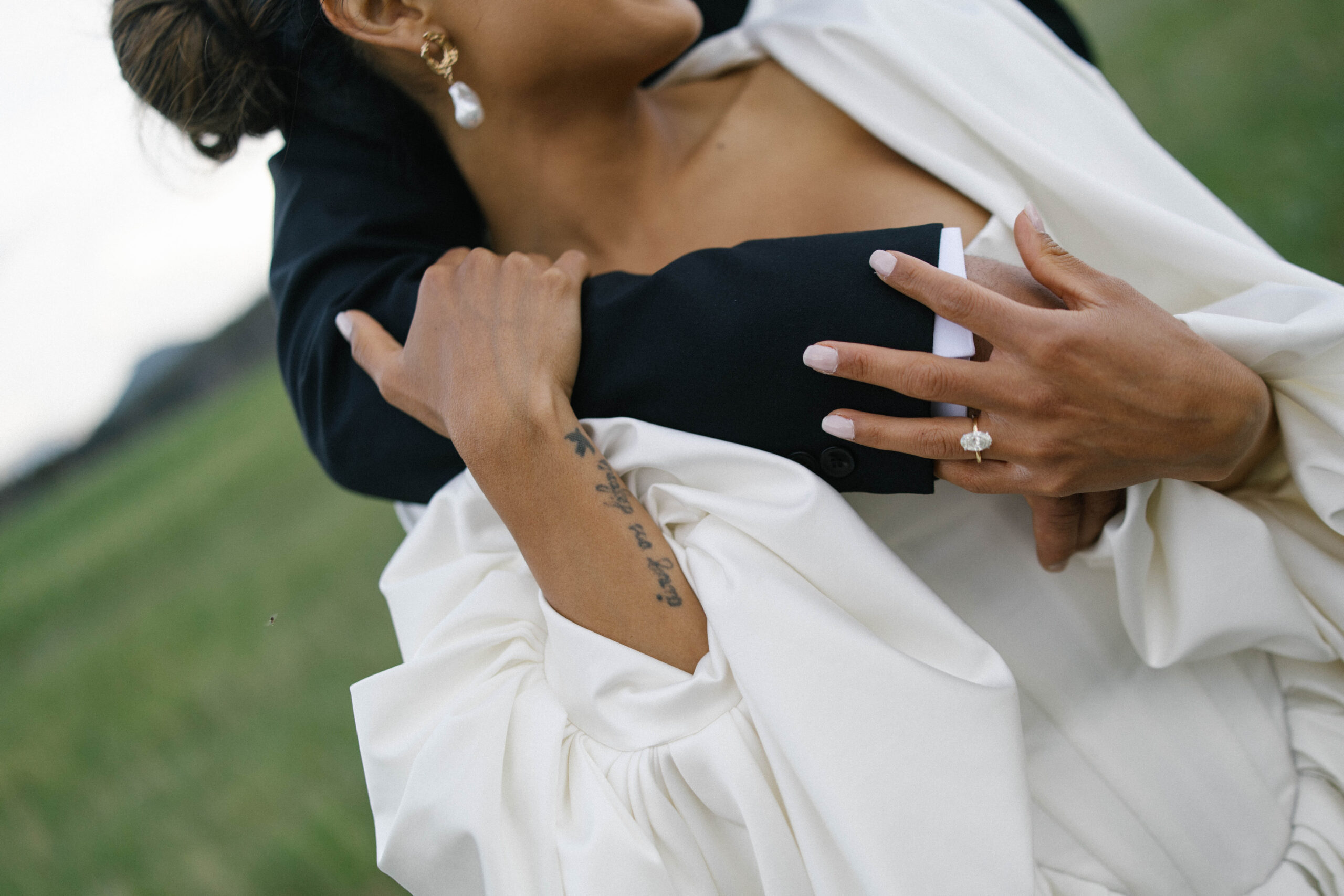 Close-up of the bride holding her partner’s arm, showing her engagement ring and pearl earrings.