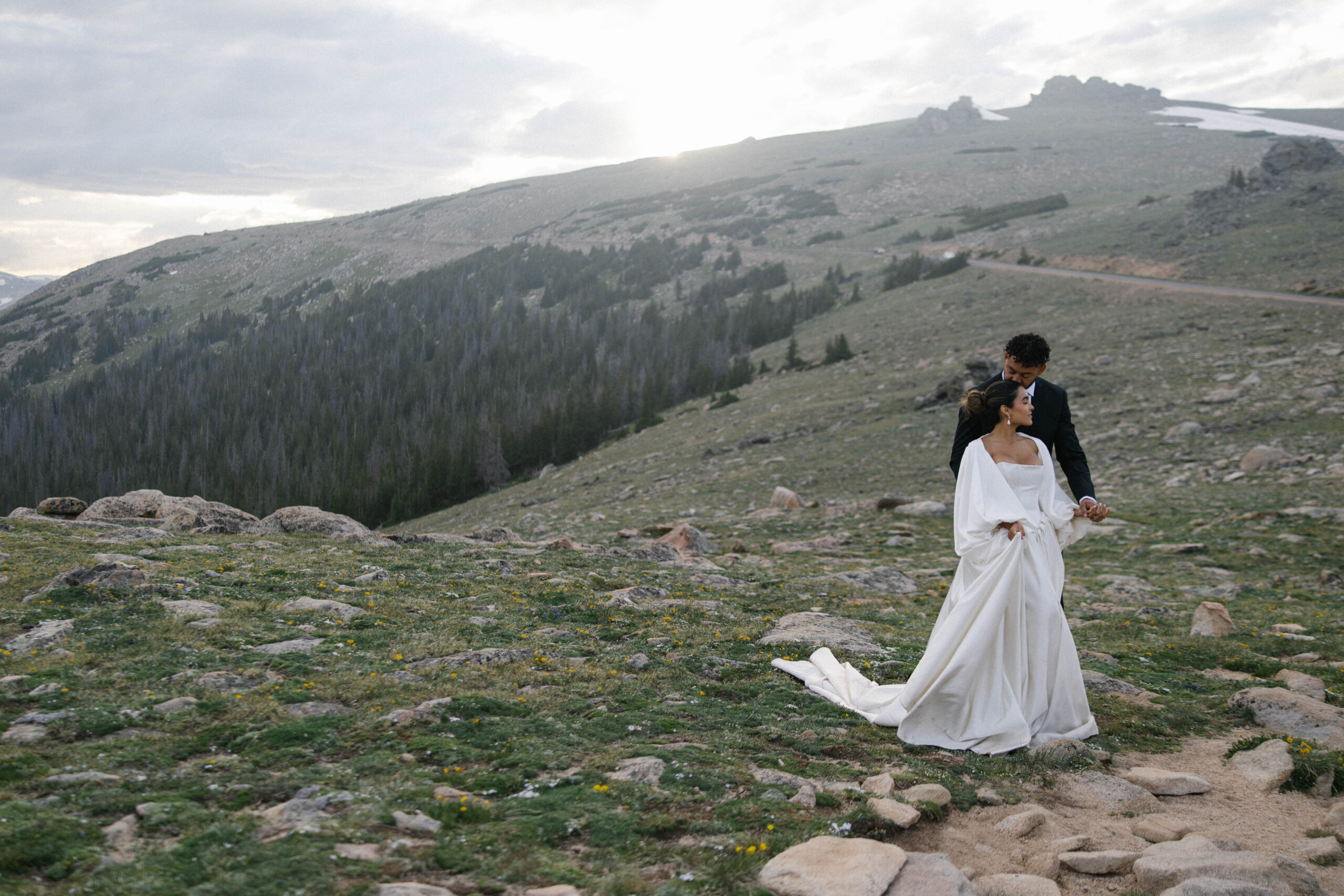 Bride and groom holding hands on a rocky hillside as the sun sets behind the ridge.