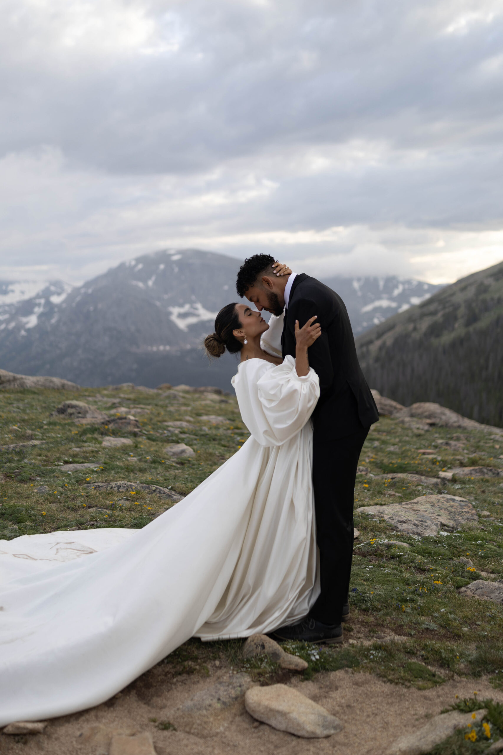 Romantic embrace between the bride and groom on a rocky mountain overlook with dramatic cloudy skies.